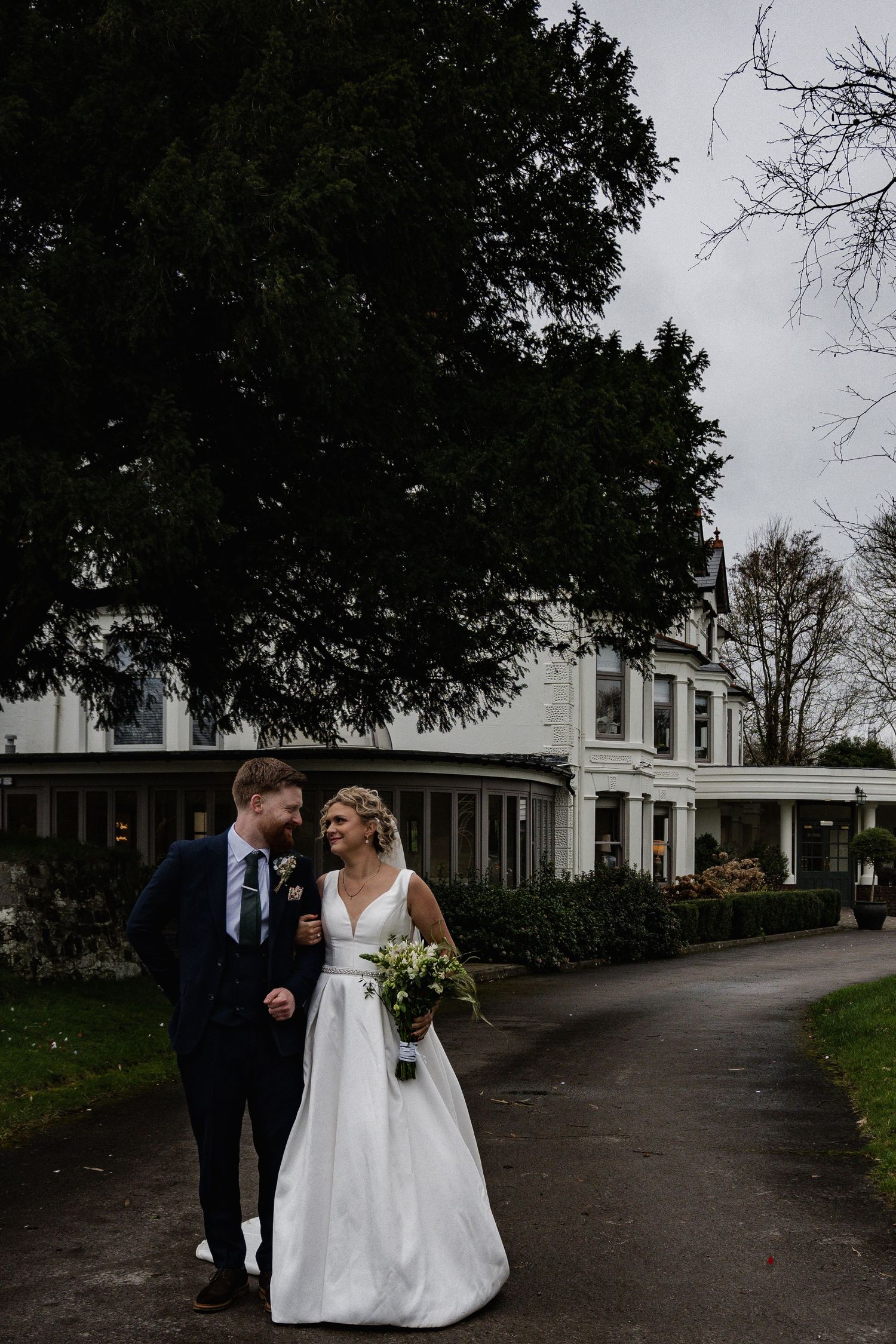 Bride and groom walking hand in hand outside a white country house wedding venue.
