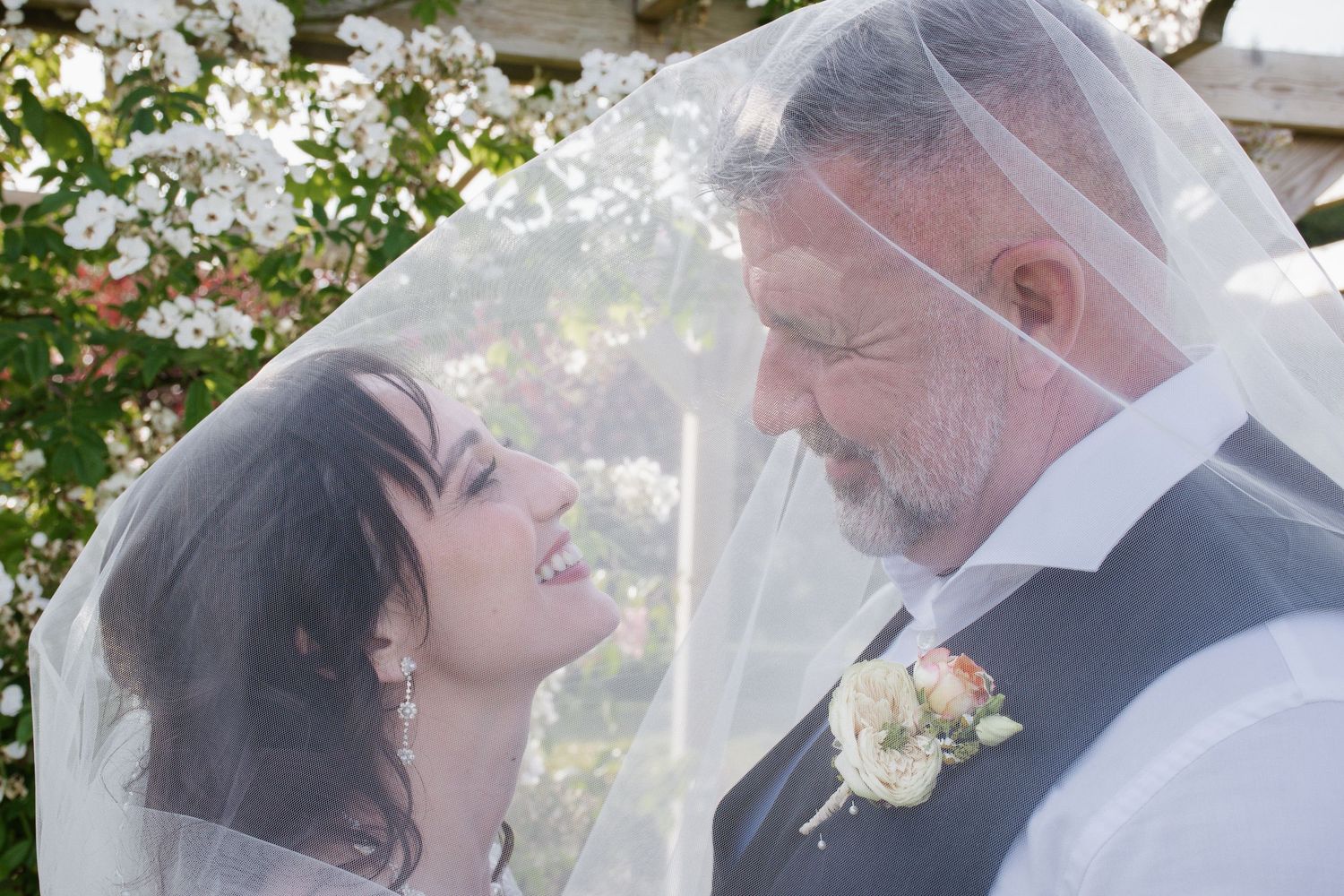Bride and groom sharing an intimate moment under a veil surrounded by blooming flowers.