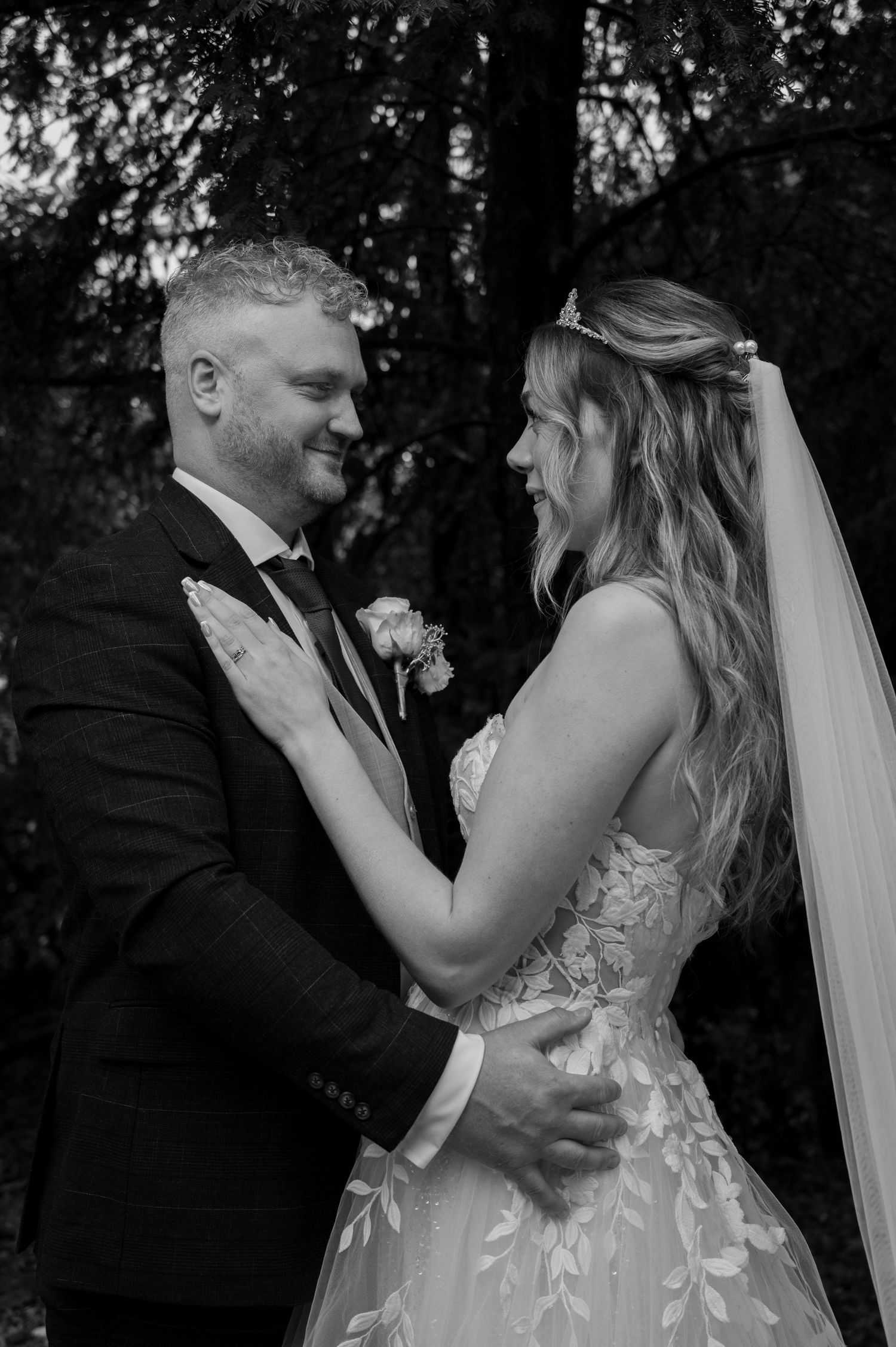 Black and white wedding photo of bride and groom gazing lovingly at each other outdoors.