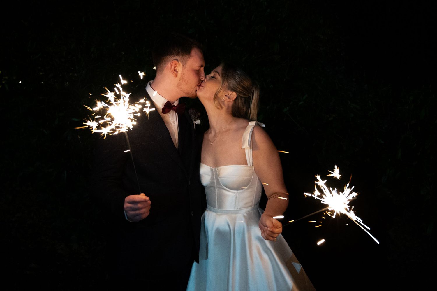 Newlyweds sharing a romantic kiss surrounded by sparklers on their wedding night.