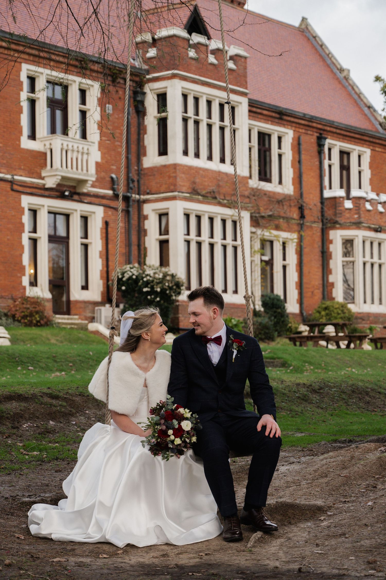 Bride and groom sit together outside a Victorian red brick manor house on their wedding day.