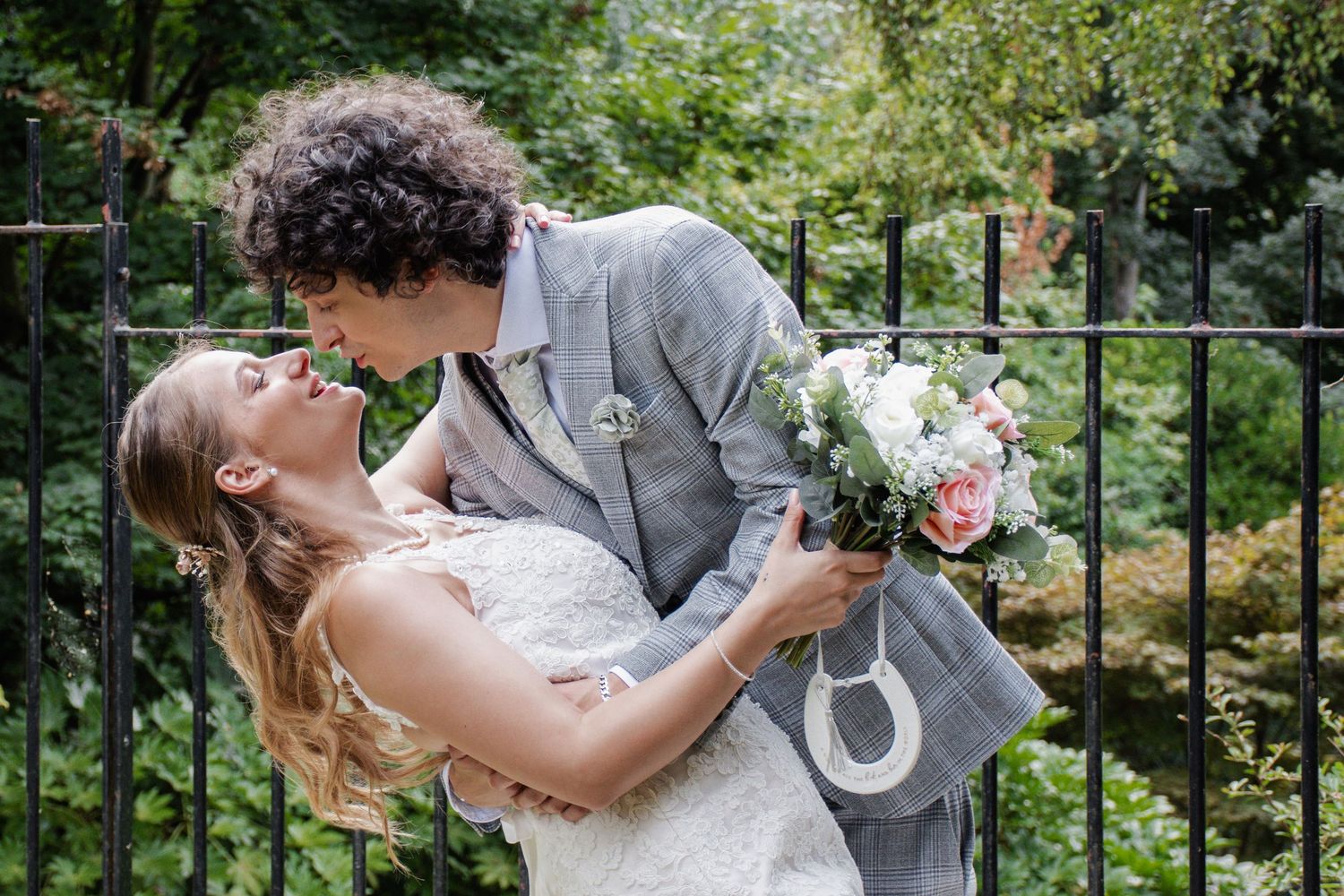 A groom dips his bride as they share a romantic moment in front of a black iron fence.