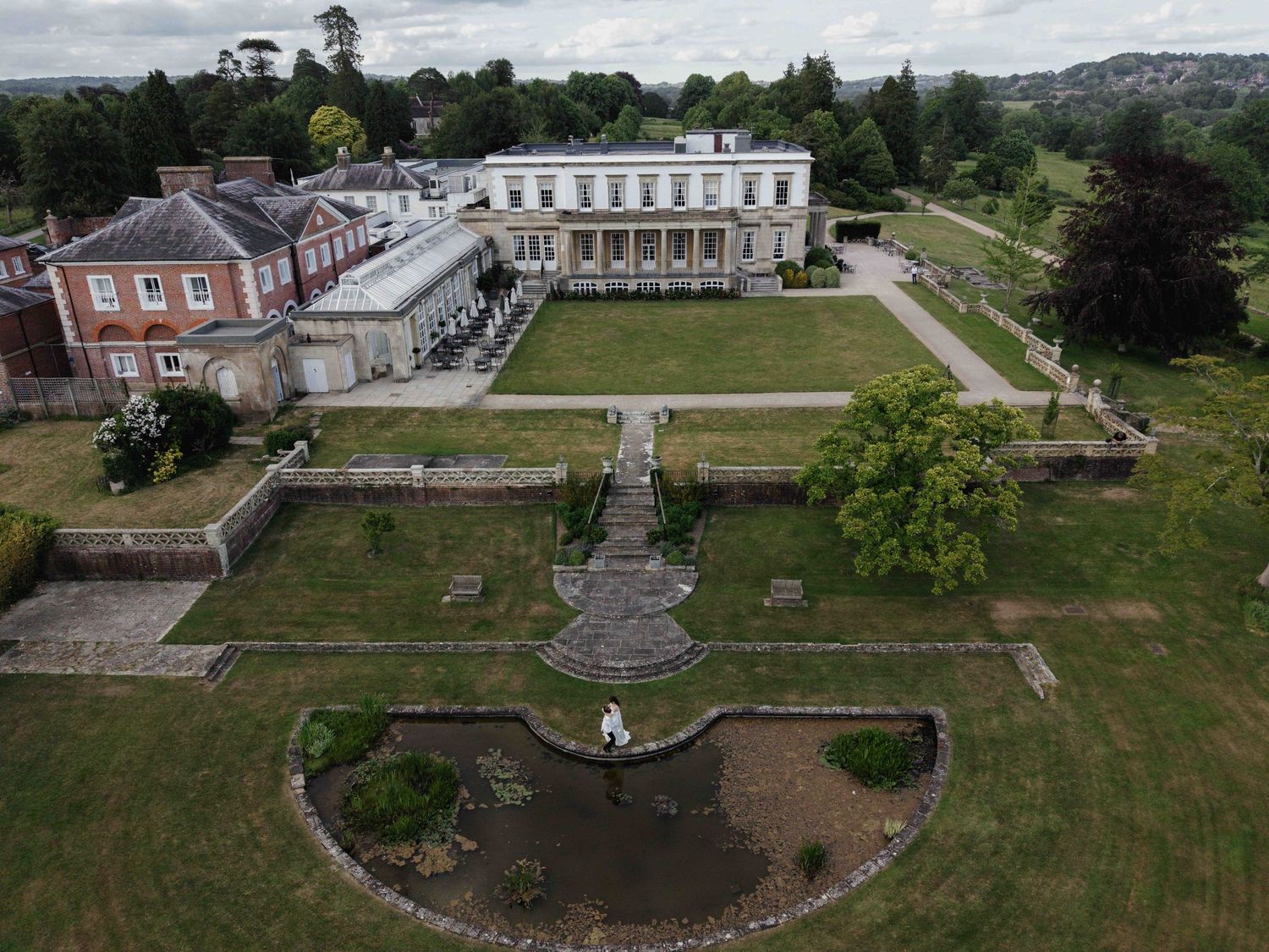 Aerial view of a stately Georgian manor with formal gardens, ornamental pond, and sweeping countryside views. Buxted Park Hotel