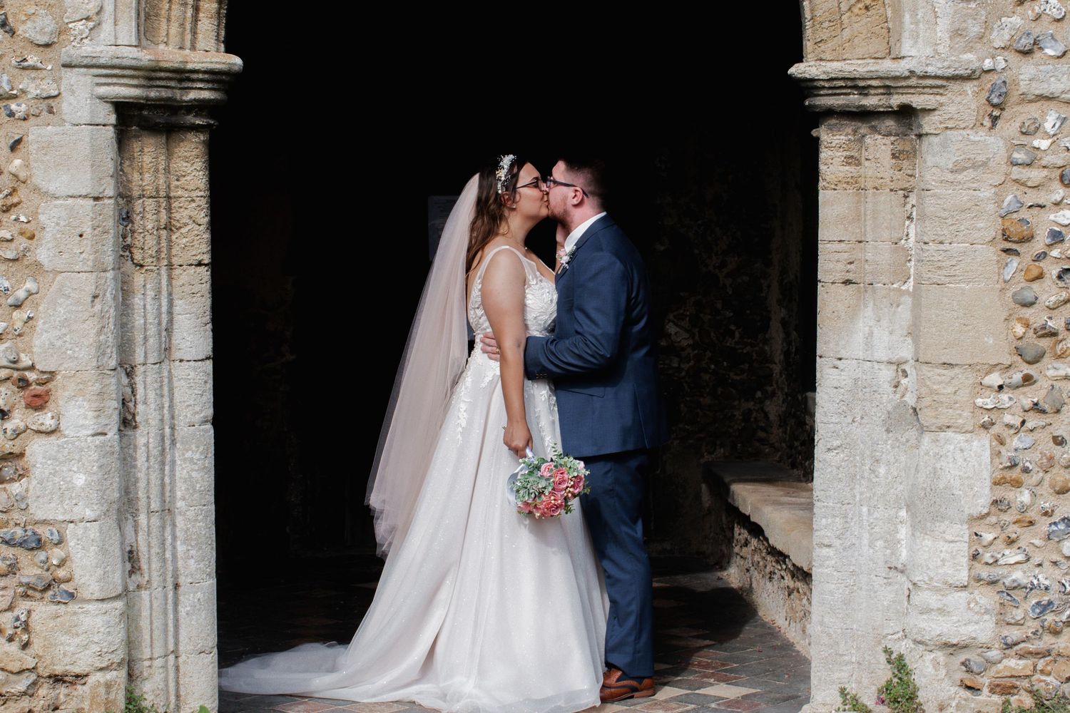 A bride and groom share an intimate moment in a rustic stone archway on their wedding day.