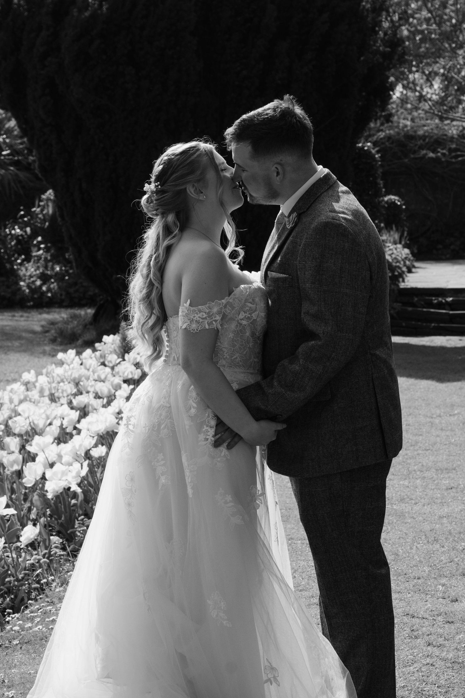 Black and white photo of bride and groom embracing tenderly in a flower garden on their wedding day.