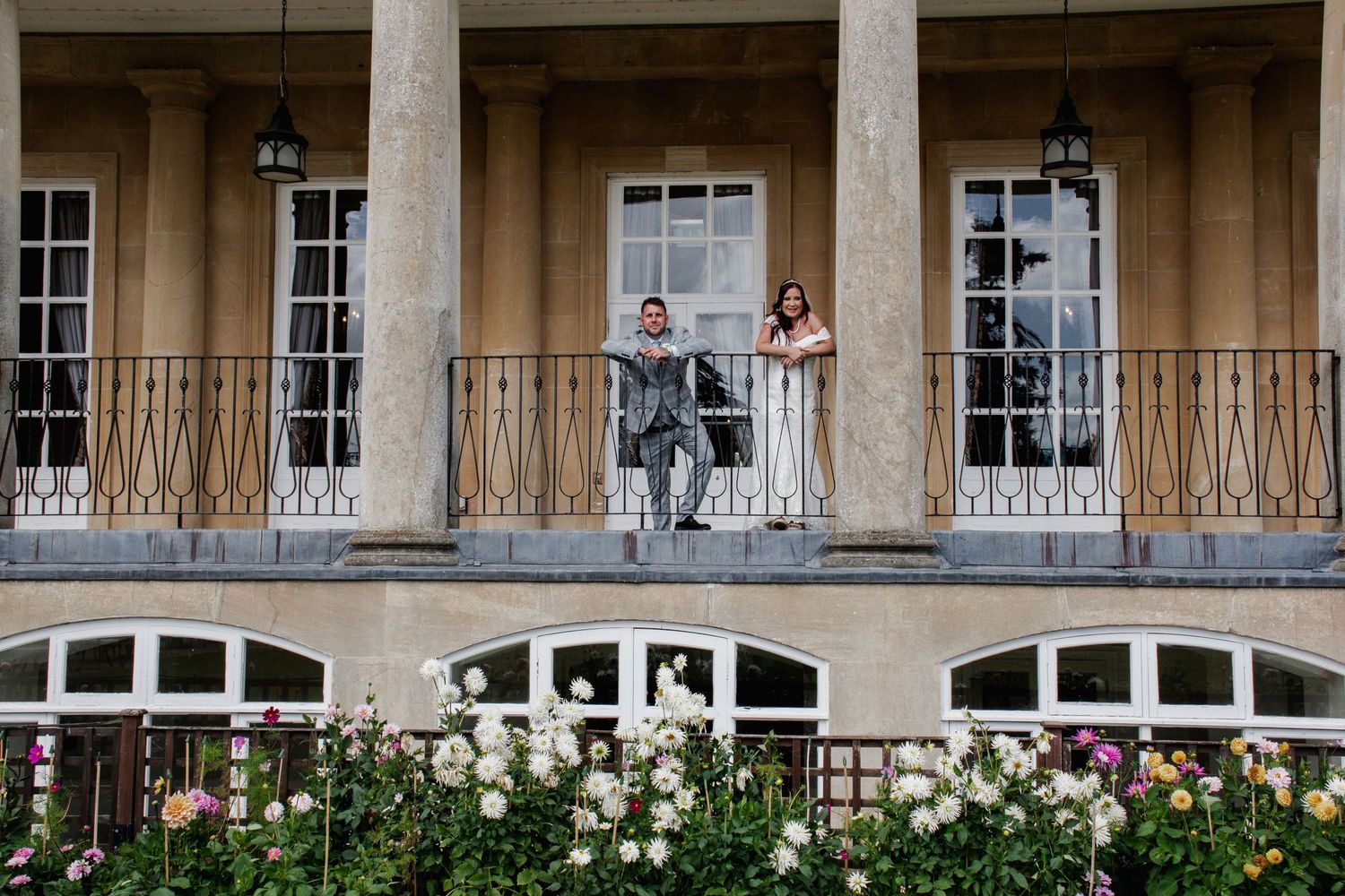 A bride and groom stand on an elegant balcony adorned with roses at their wedding venue.