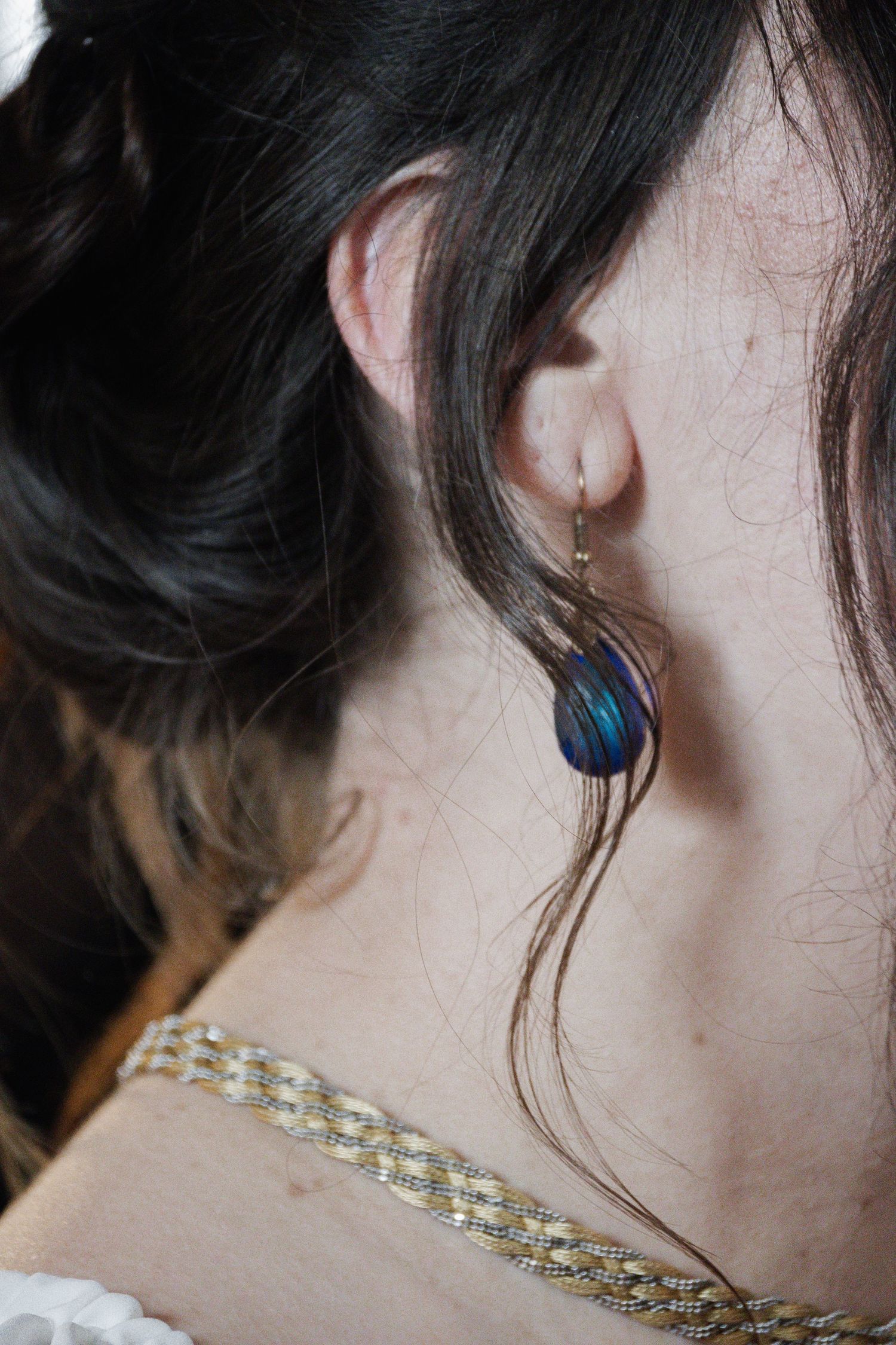 Close-up of bride wearing elegant blue feather drop earrings and a delicate gold chain necklace on her wedding day.
