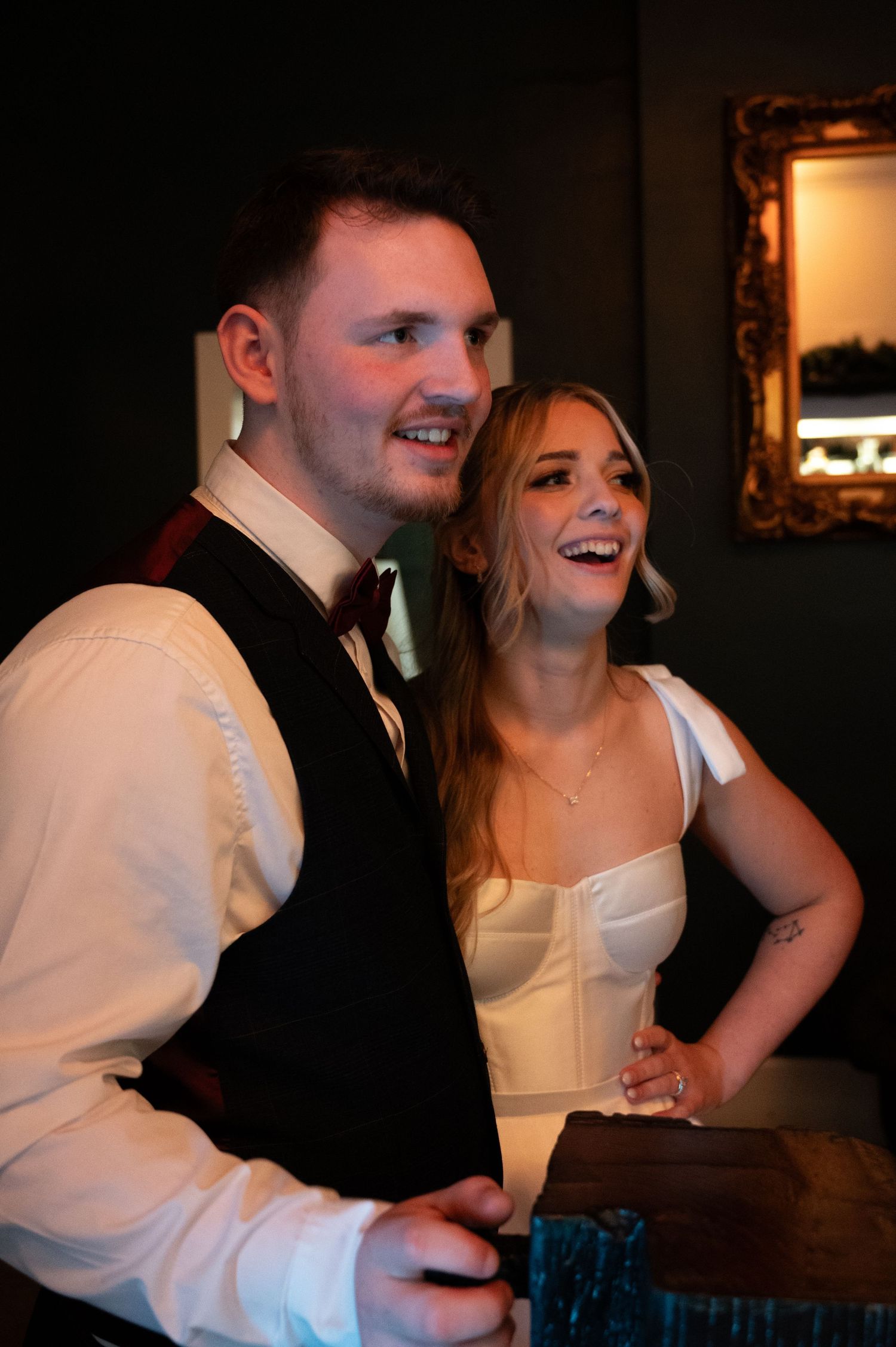 Bride and groom laughing together at their wedding reception in a warmly lit venue.