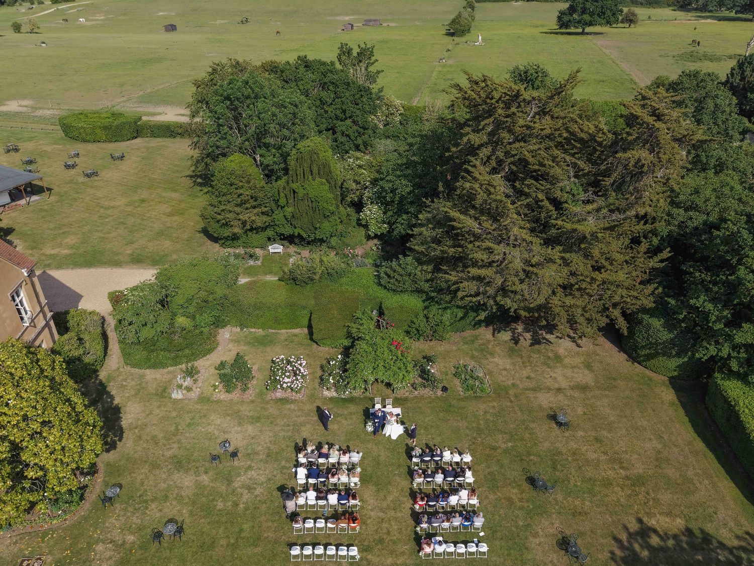 Aerial view of an outdoor wedding ceremony with white chairs arranged on a green estate lawn. Nursted Court
