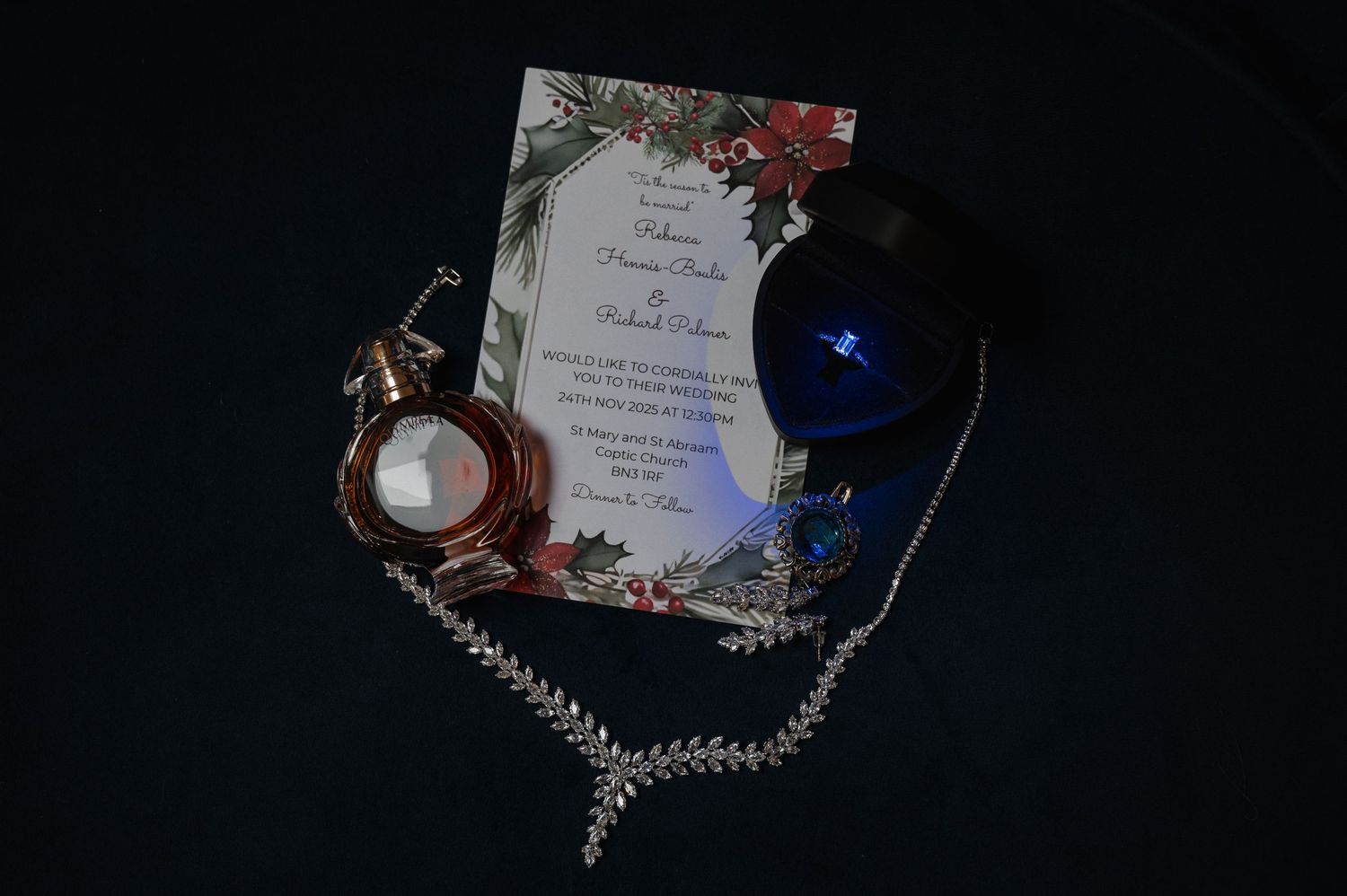 Wedding flat lay featuring floral invitation, diamond necklace, perfume bottle, and blue ornament.