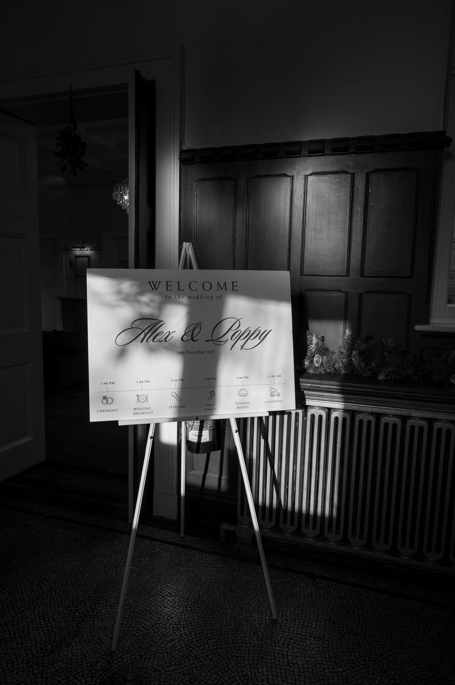 Black and white welcome sign for Alex and Poppys wedding day displayed on an easel.