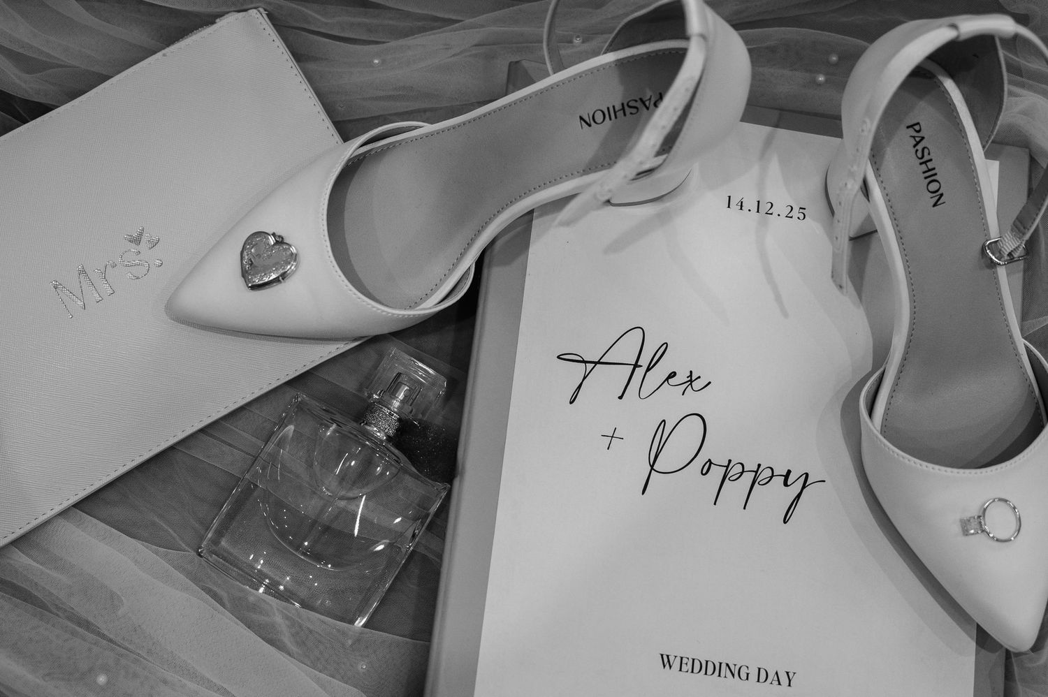 Black and white flat lay of wedding details including shoes, rings, and Alex and Poppy program.