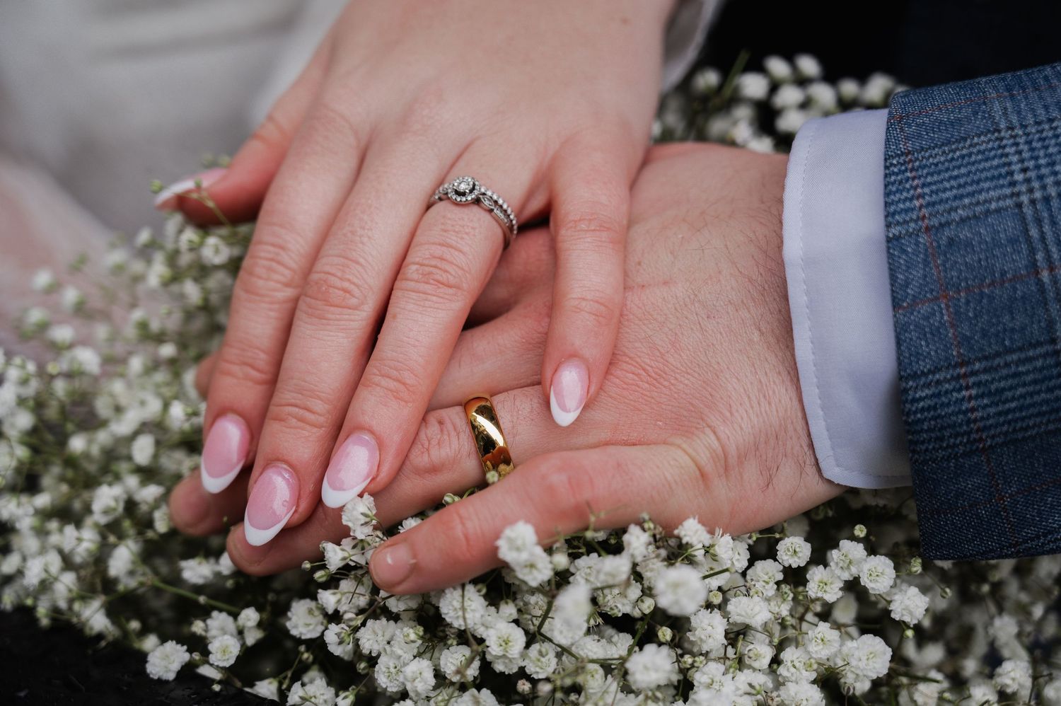 Close-up of newlyweds hands displaying wedding rings resting on white baby's breath flowers.