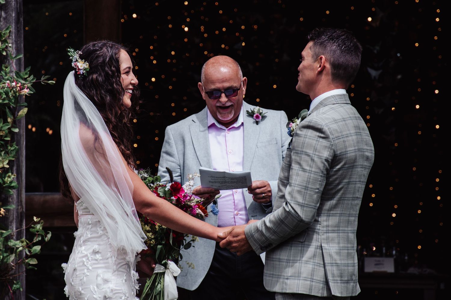 Bride and groom exchanging vows with celebrant at a twinkling star backdrop wedding ceremony. The cEDAR rOOF bARN