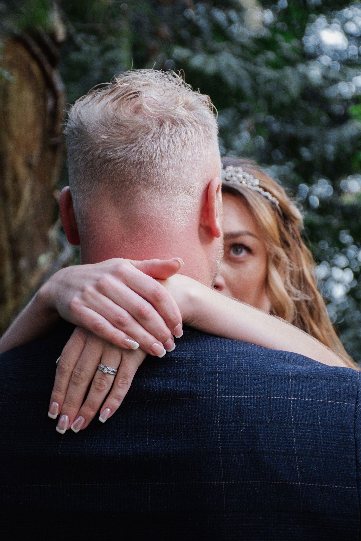 Close-up of bride hugging groom showing diamond wedding ring on her hand at outdoor wedding.