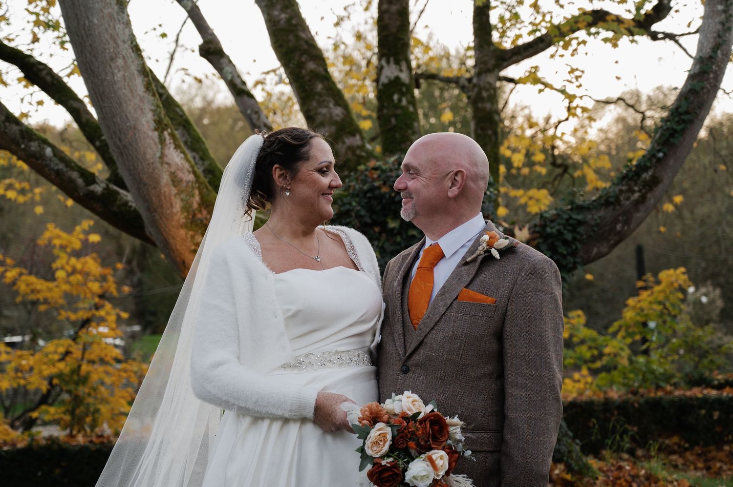 Bride and groom sharing a loving glance surrounded by golden autumn trees in a romantic outdoor wedding portrait.