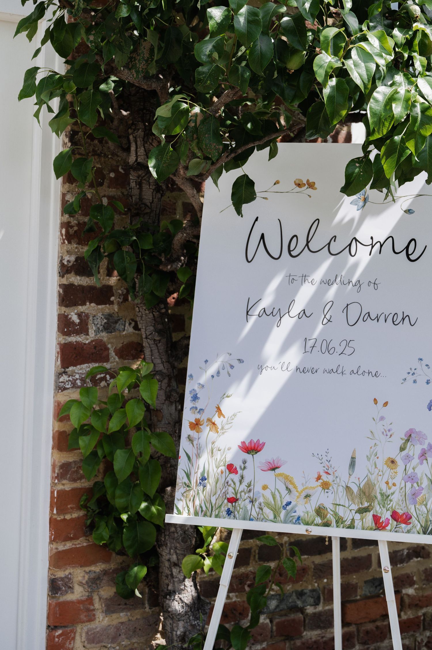 Welcome wedding sign for Kayla and Darren dated 17.06.25 decorated with wildflowers on easel.
