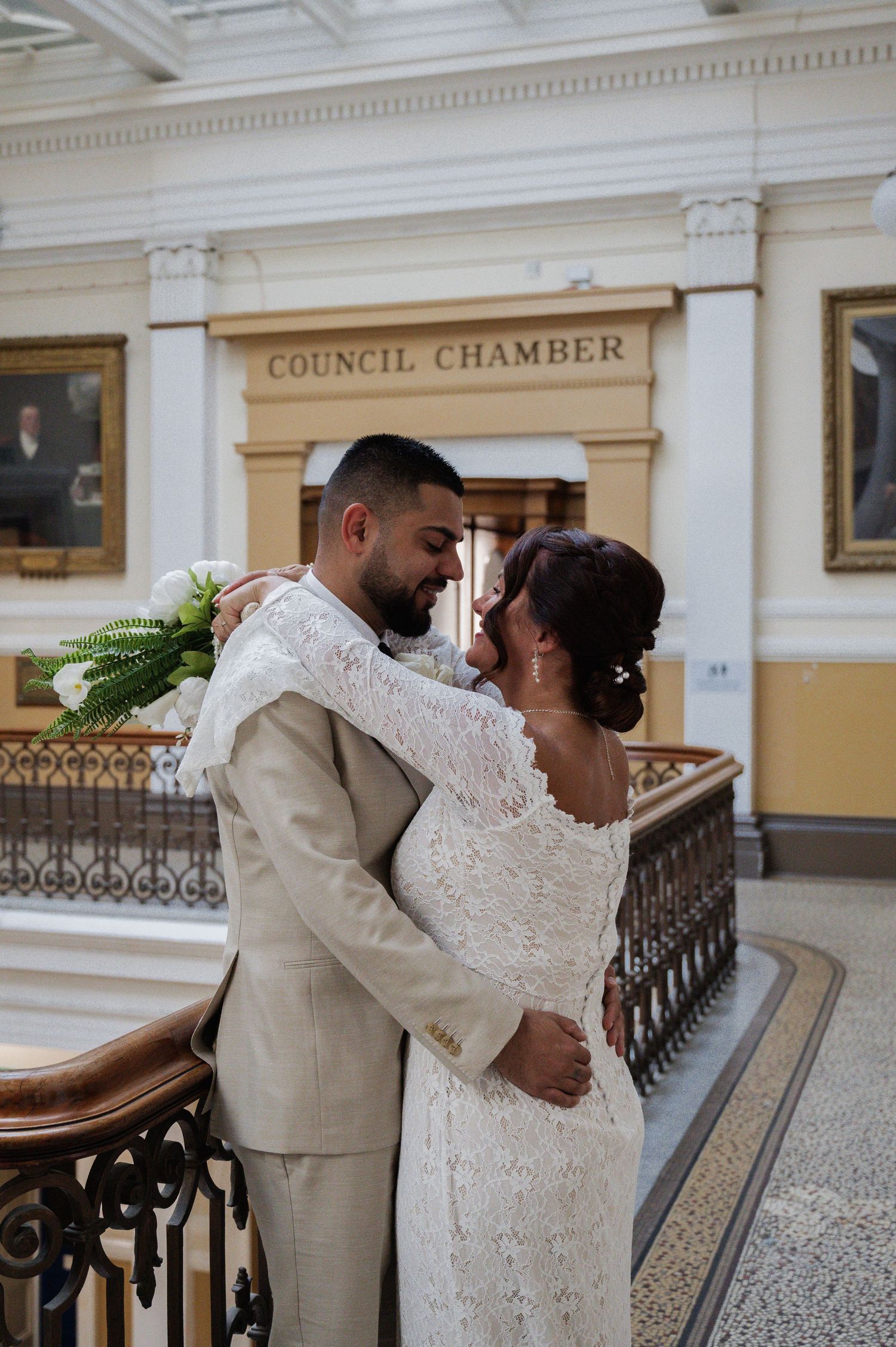 Bride and groom embracing romantically on staircase outside Council Chamber wedding venue.