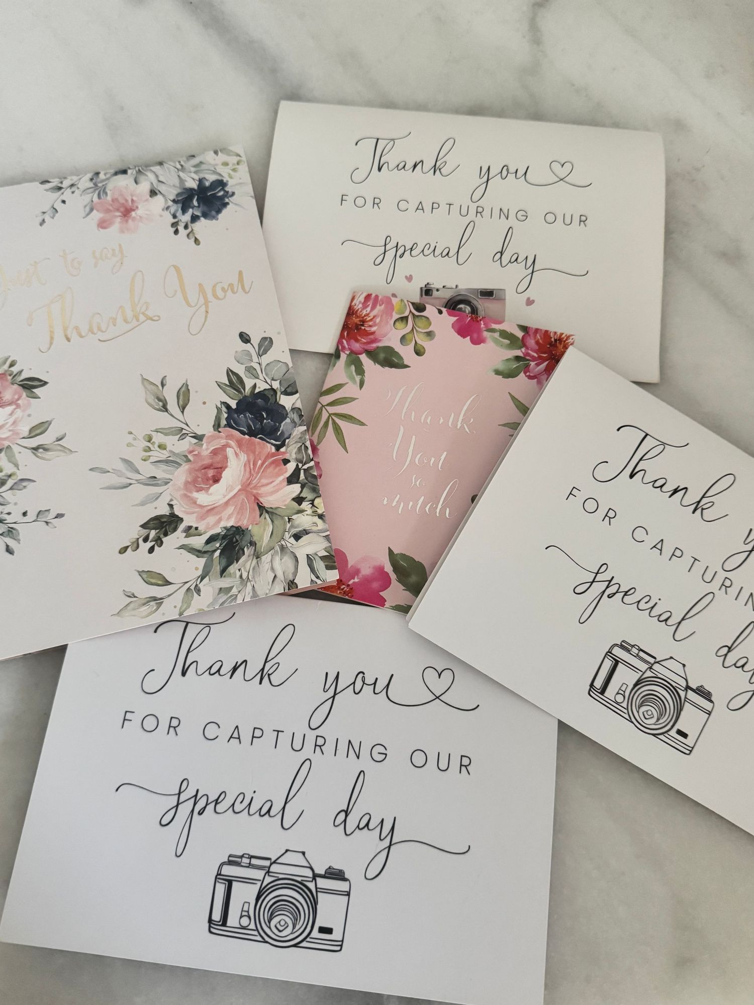 Collection of floral and elegant thank you cards for wedding photographers arranged on marble surface.