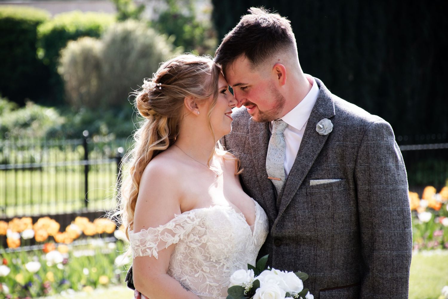 Romantic couple in a sunny garden, bride in lace off-shoulder gown and groom in grey tweed suit. Lewes Registry Office