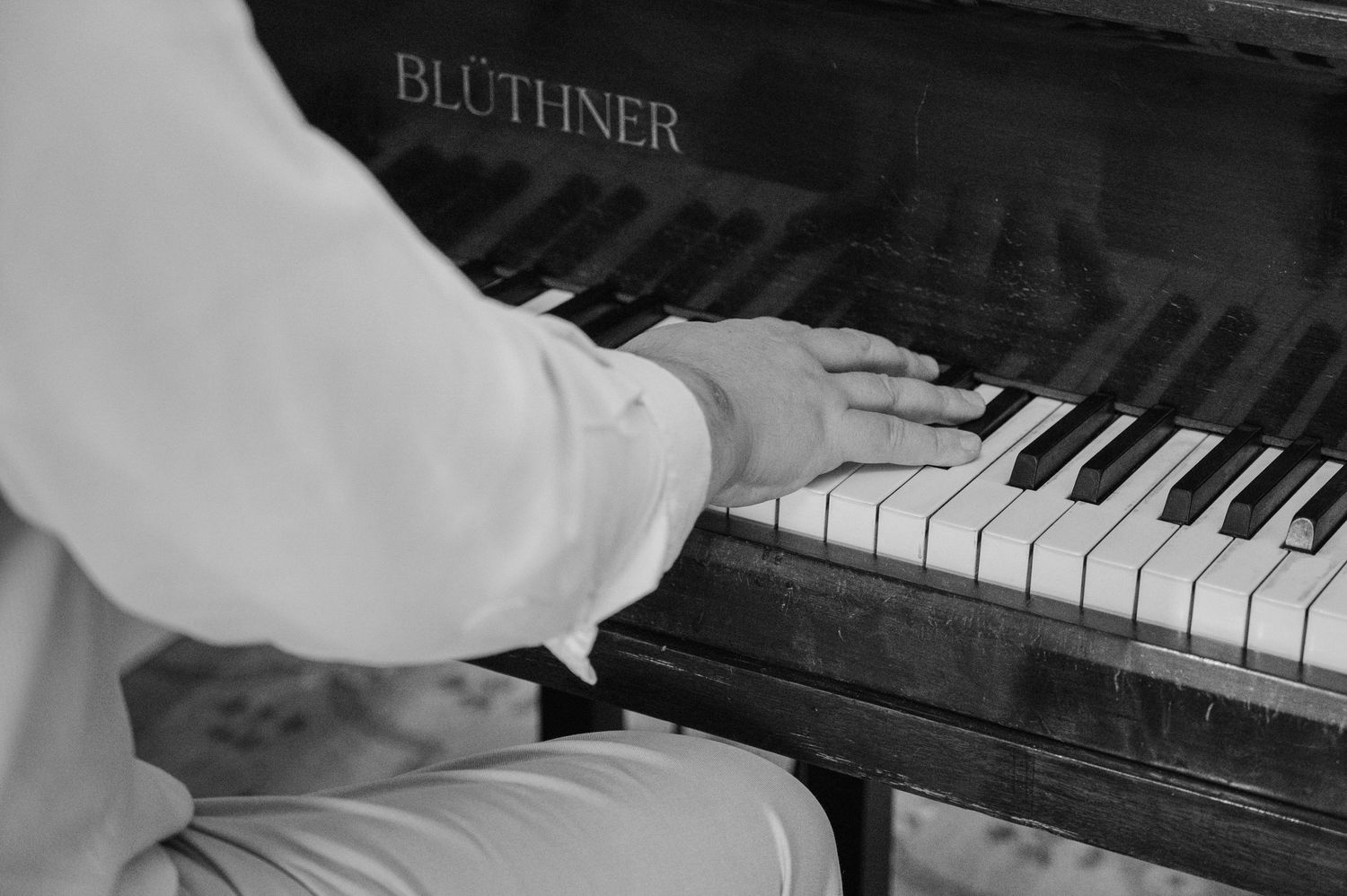 Black and white close-up of hands playing a Bluthner grand piano at a wedding reception.