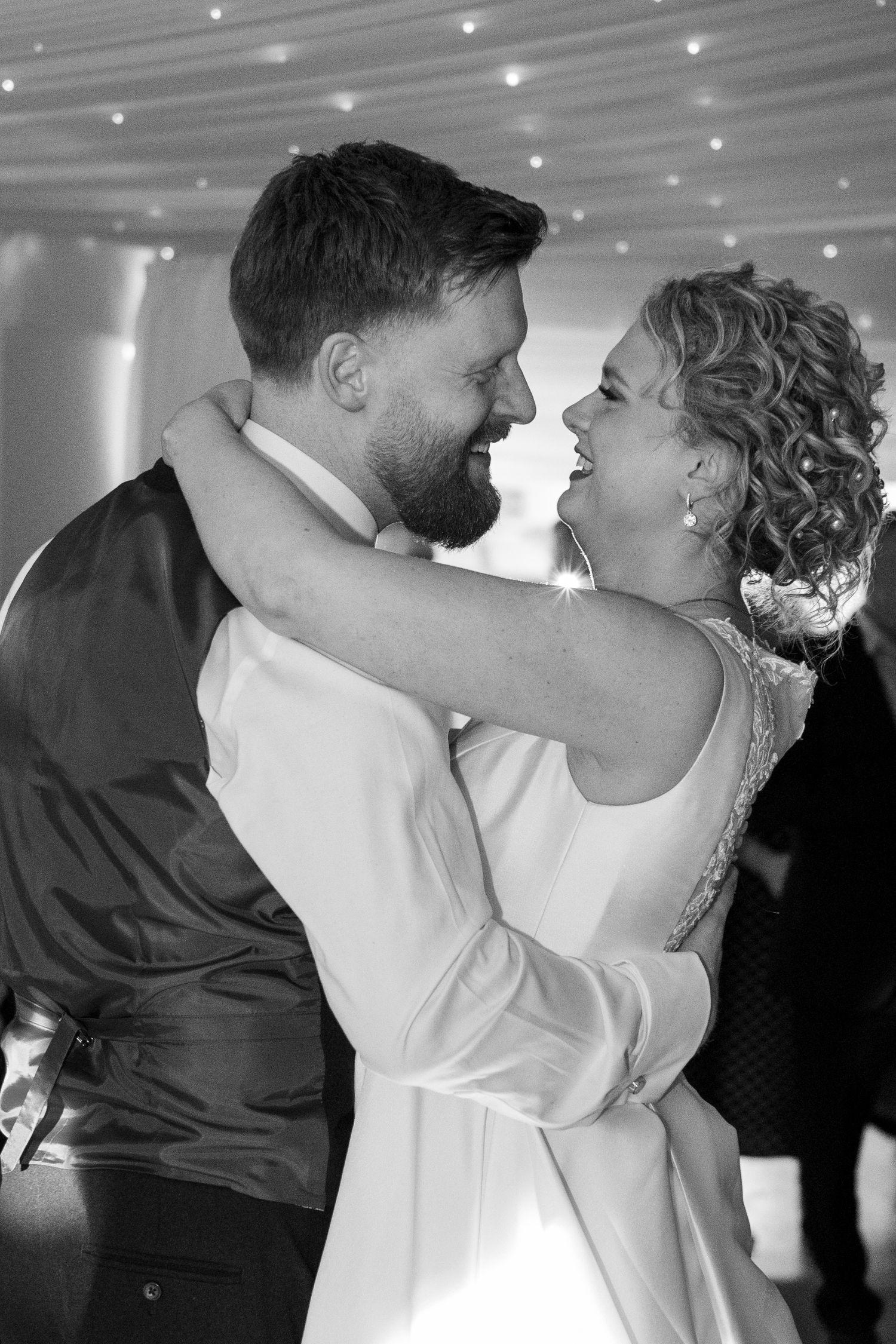 Black and white photo of a bride and groom sharing a joyful first dance embrace.