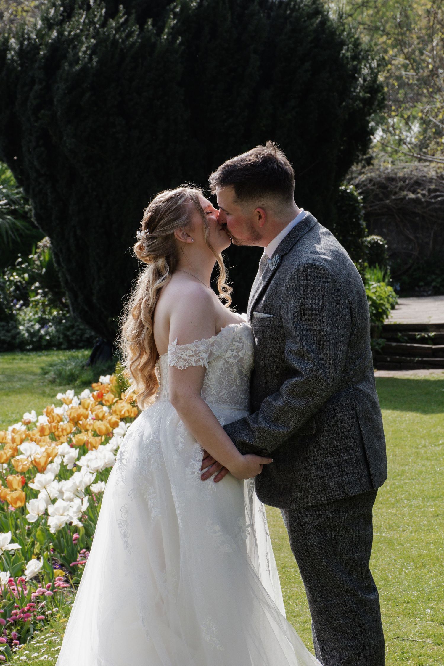 Bride and groom sharing a romantic kiss in a garden with colorful tulips blooming in the background.