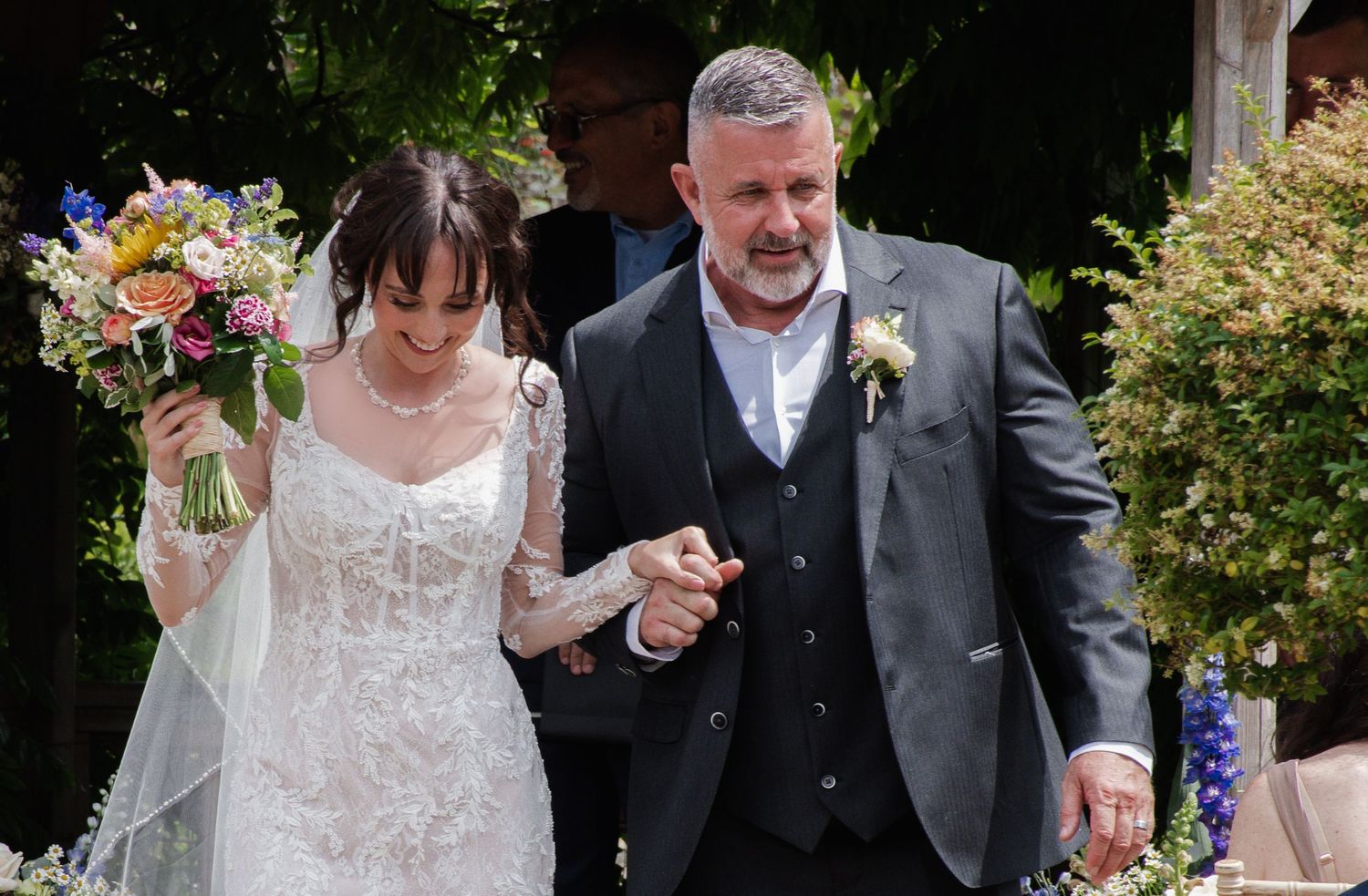 Bride and groom walking hand in hand outdoors, bride holding colorful bouquet. Secret Garden