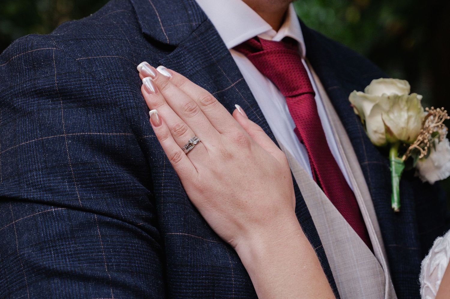 Close-up of bride's hand showing diamond wedding ring resting on groom's navy checked suit.