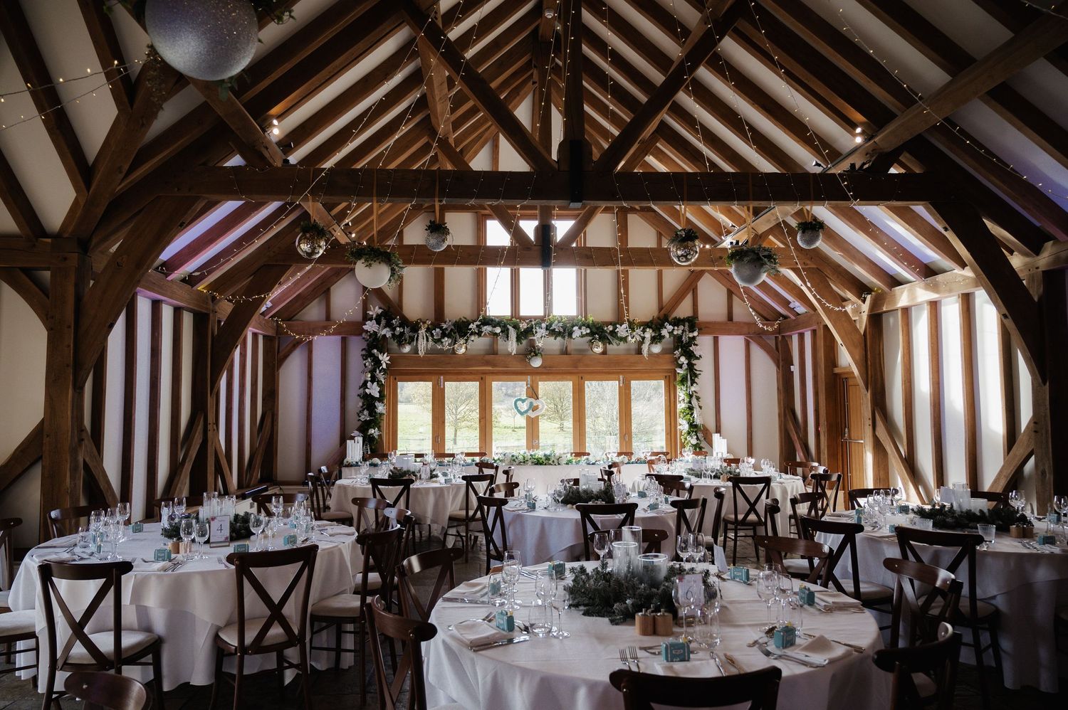Elegant barn wedding reception with wooden beamed ceiling, round tables, and floral arch backdrop.