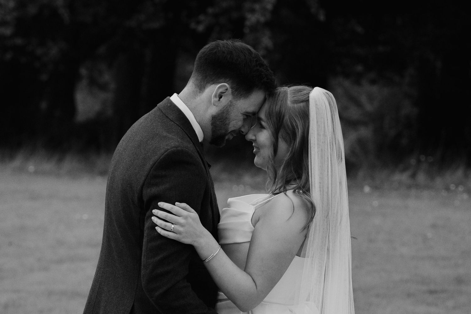 Intimate black and white portrait of bride and groom touching foreheads tenderly in a garden setting.