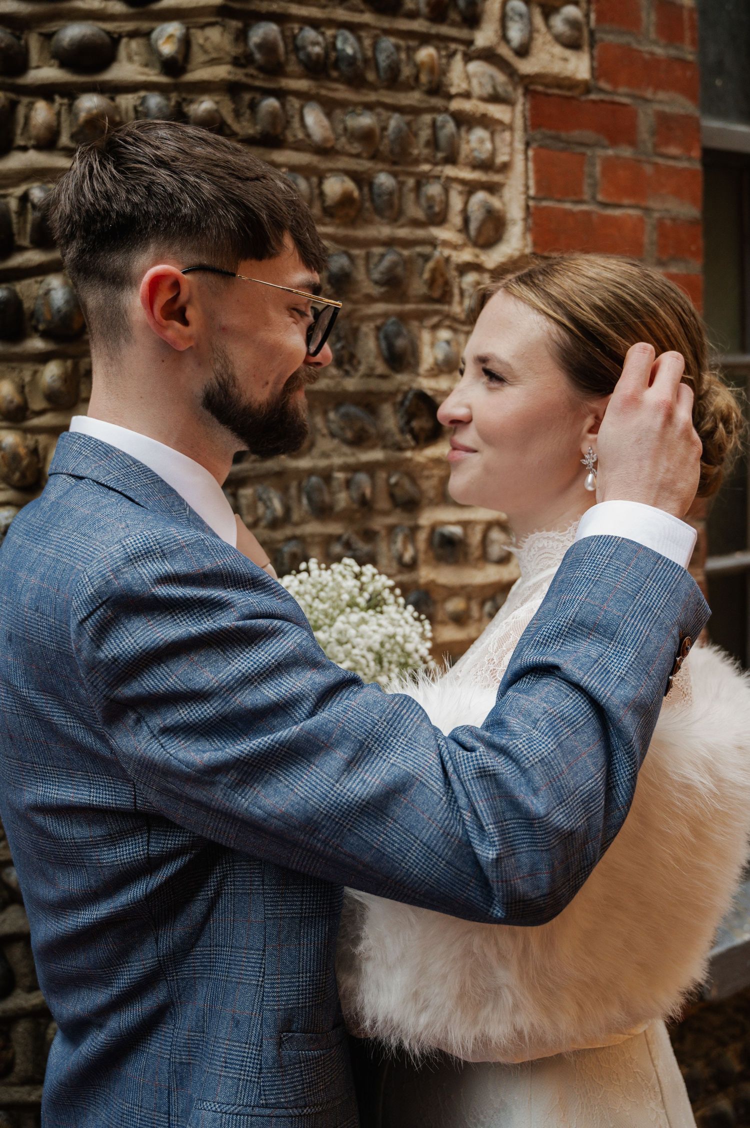 Groom in blue tweed suit tenderly touches bride's face as they share an intimate moment outdoors.