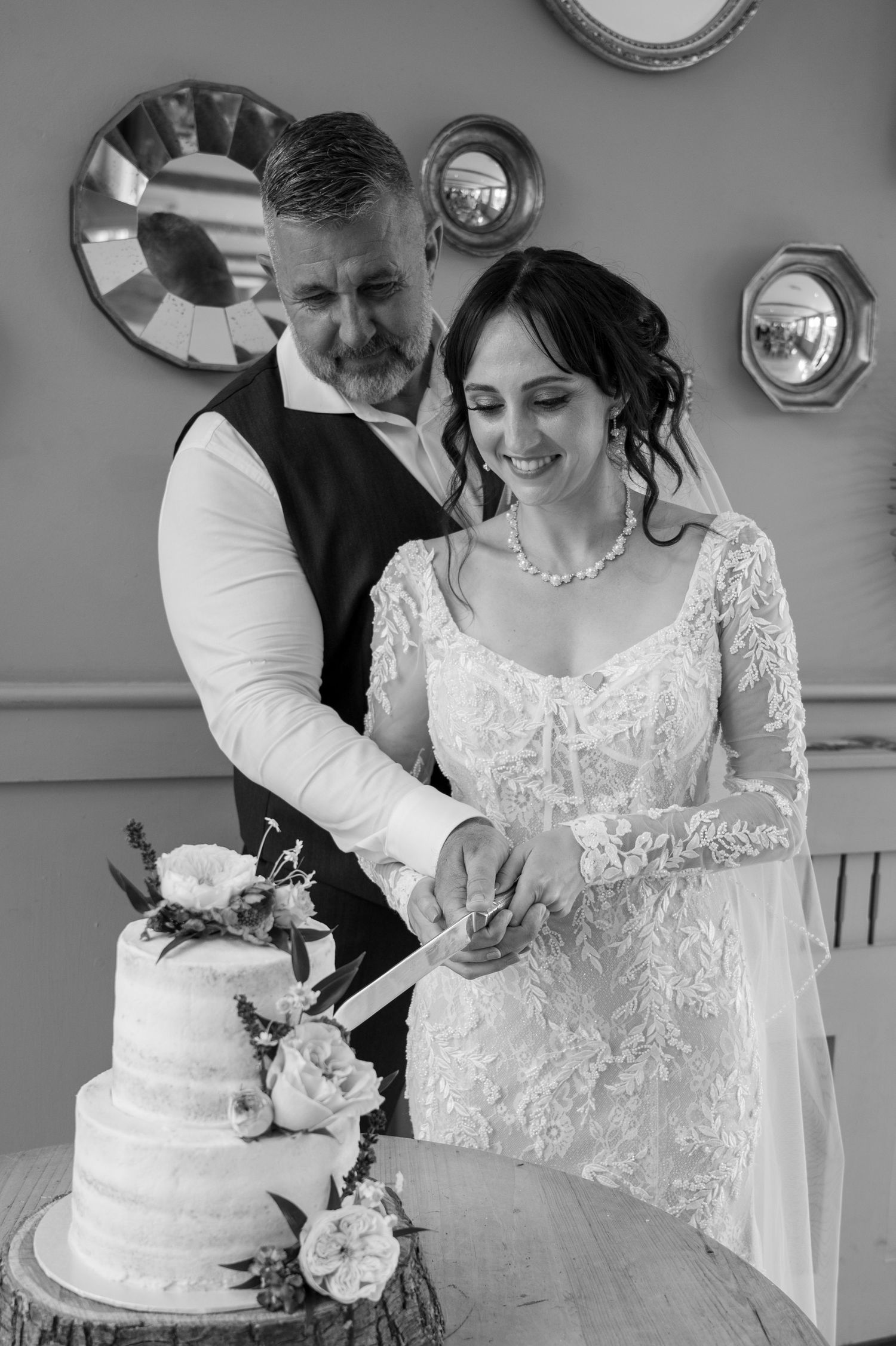 Bride and groom cutting their elegant tiered wedding cake together in black and white photo.
