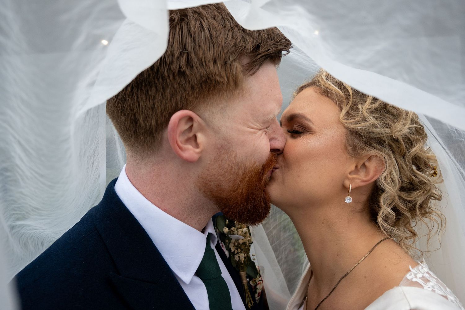 Bride and groom sharing a romantic kiss under a flowing white veil.