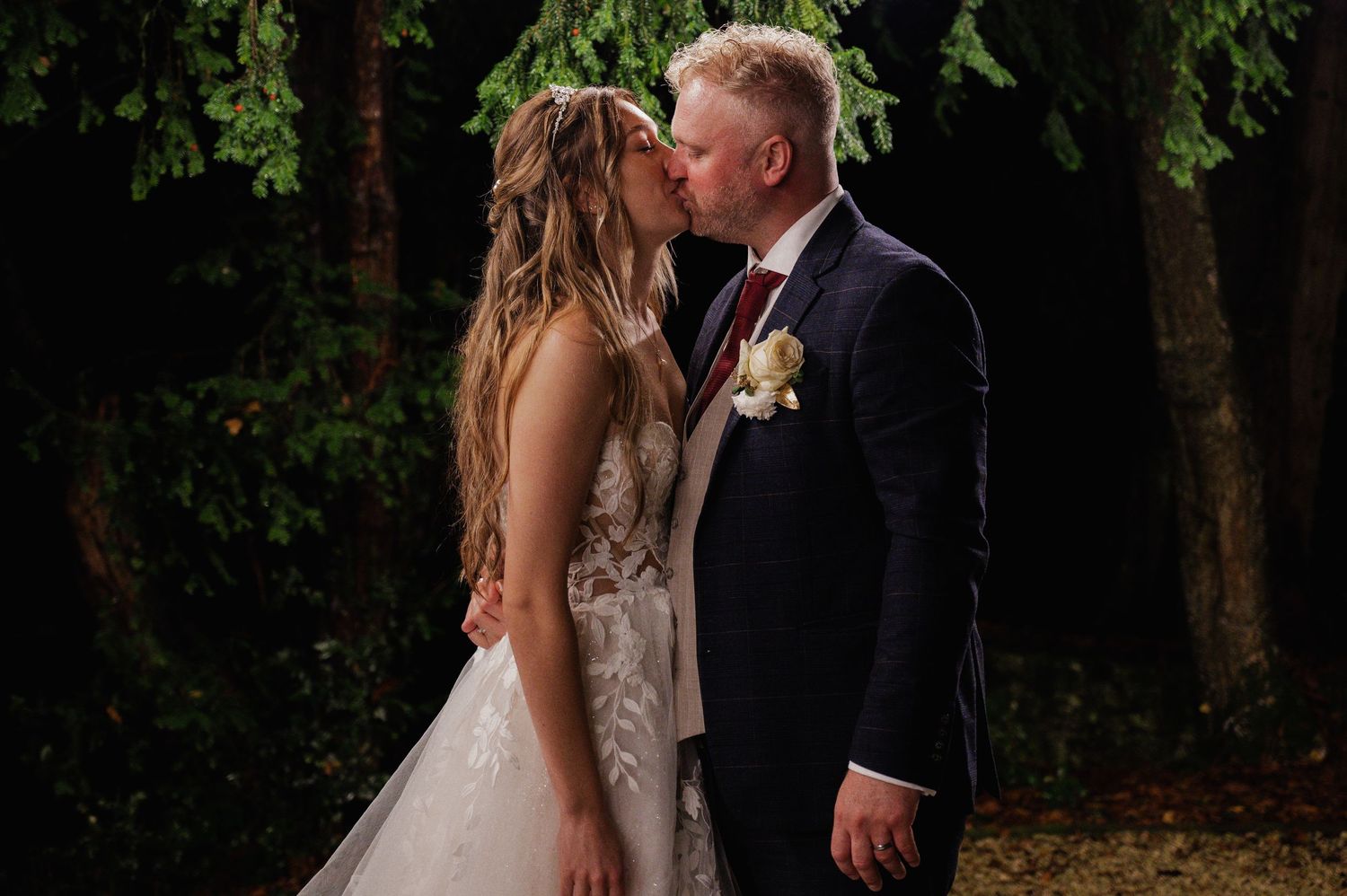 Bride and groom sharing a romantic kiss outdoors at night during their wedding celebration.