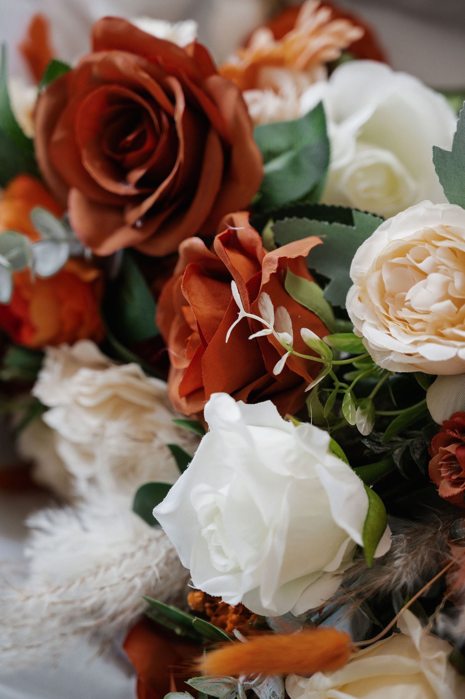 Close-up of a stunning wedding bouquet featuring burnt orange and white roses with lush green foliage accents.