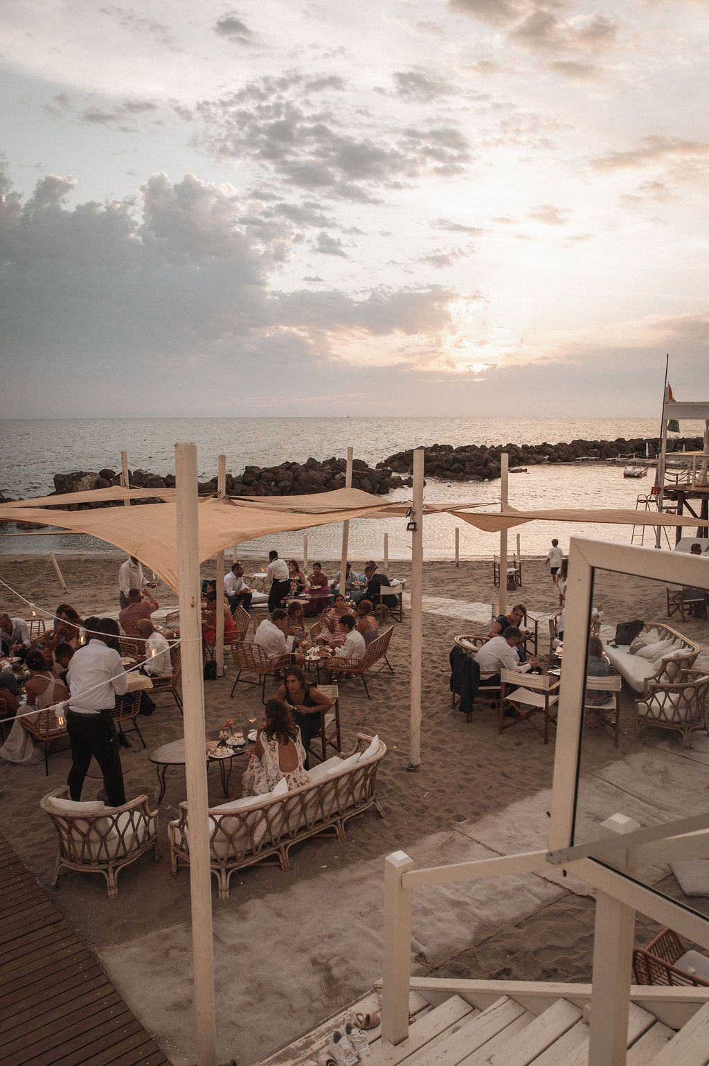 Beachside wedding reception setup with white canopy and tables at sunset.