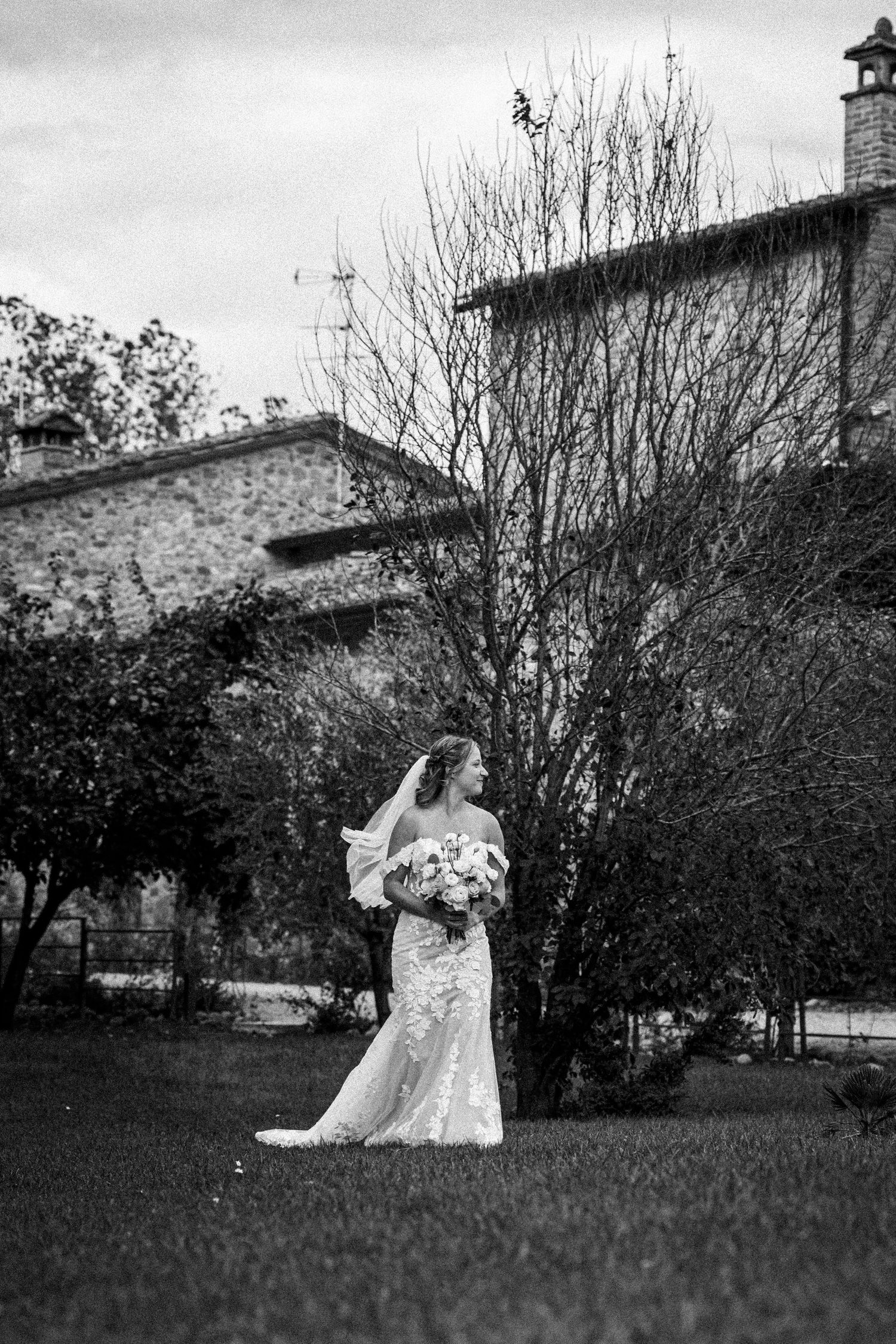 Wedding couple photographed from distance on garden lawn with stone building backdrop.