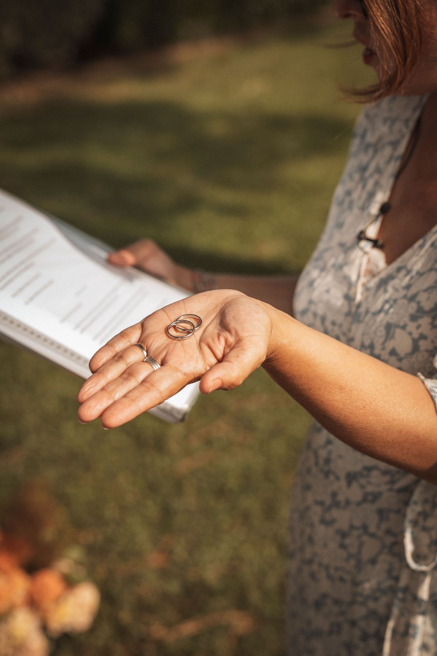 Close-up of hands holding a wedding ceremony program against a grassy outdoor background.