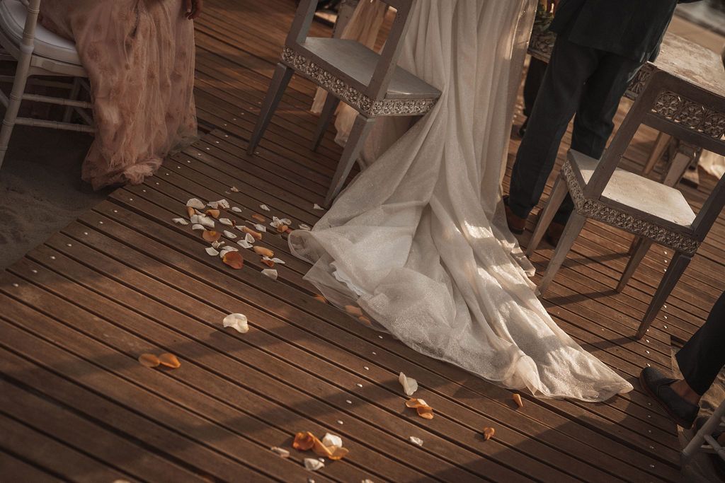 Close-up view of rose petals scattered on a wooden deck during a beach wedding ceremony.