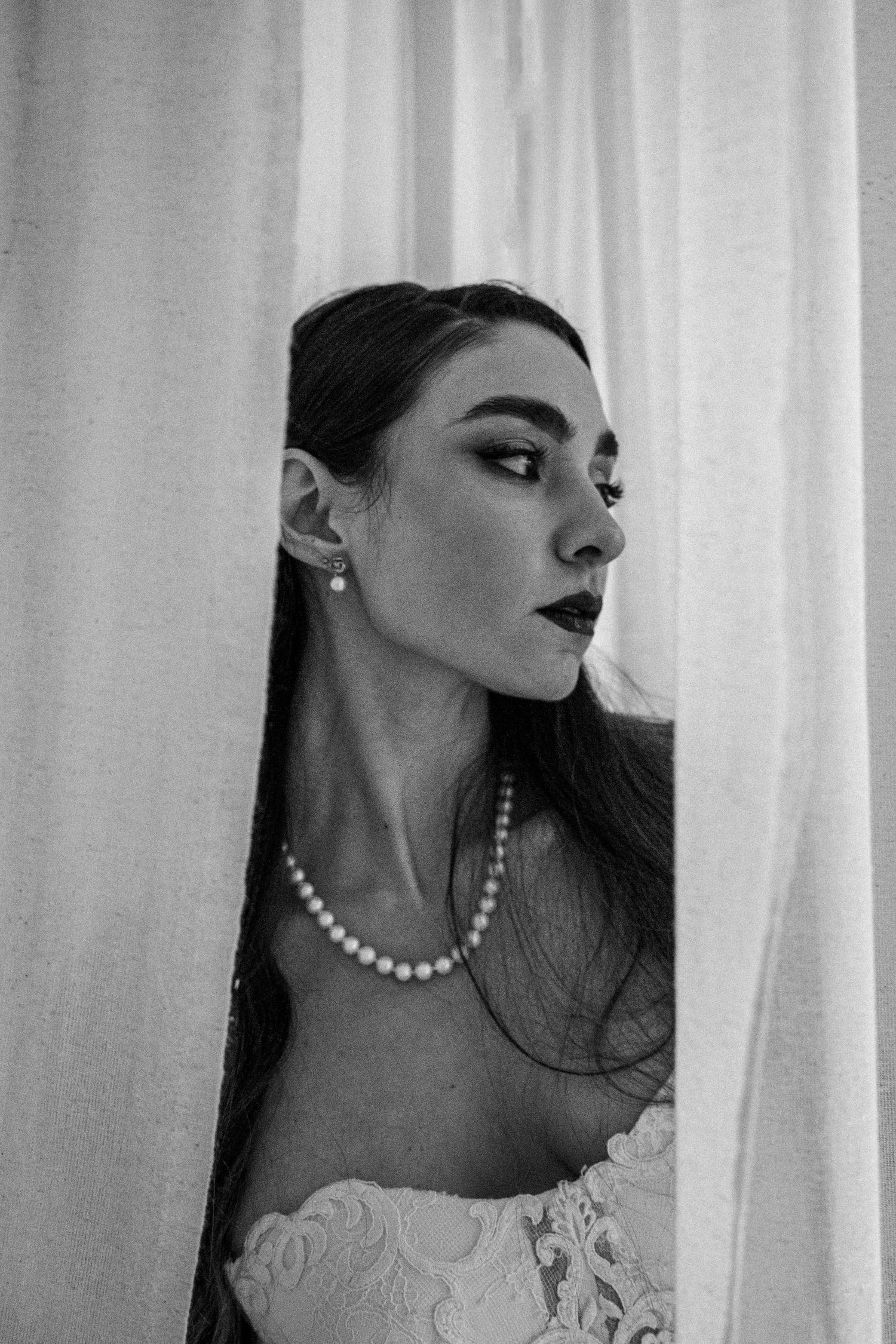 Black and white portrait of bride wearing pearl necklace and strapless gown with lace details.