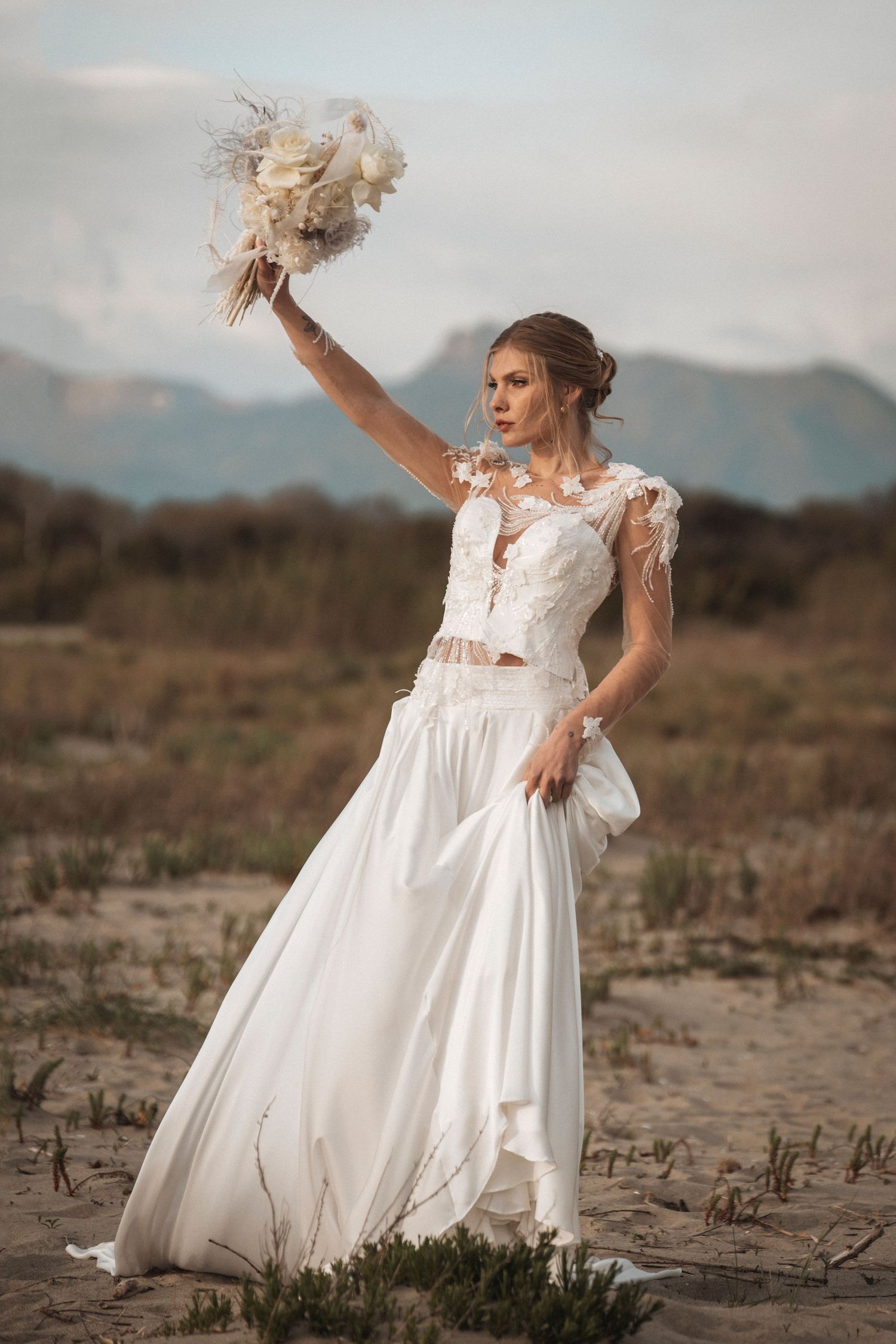 A wedding dress with delicate lace details photographed against a mountainous desert landscape at sunset.