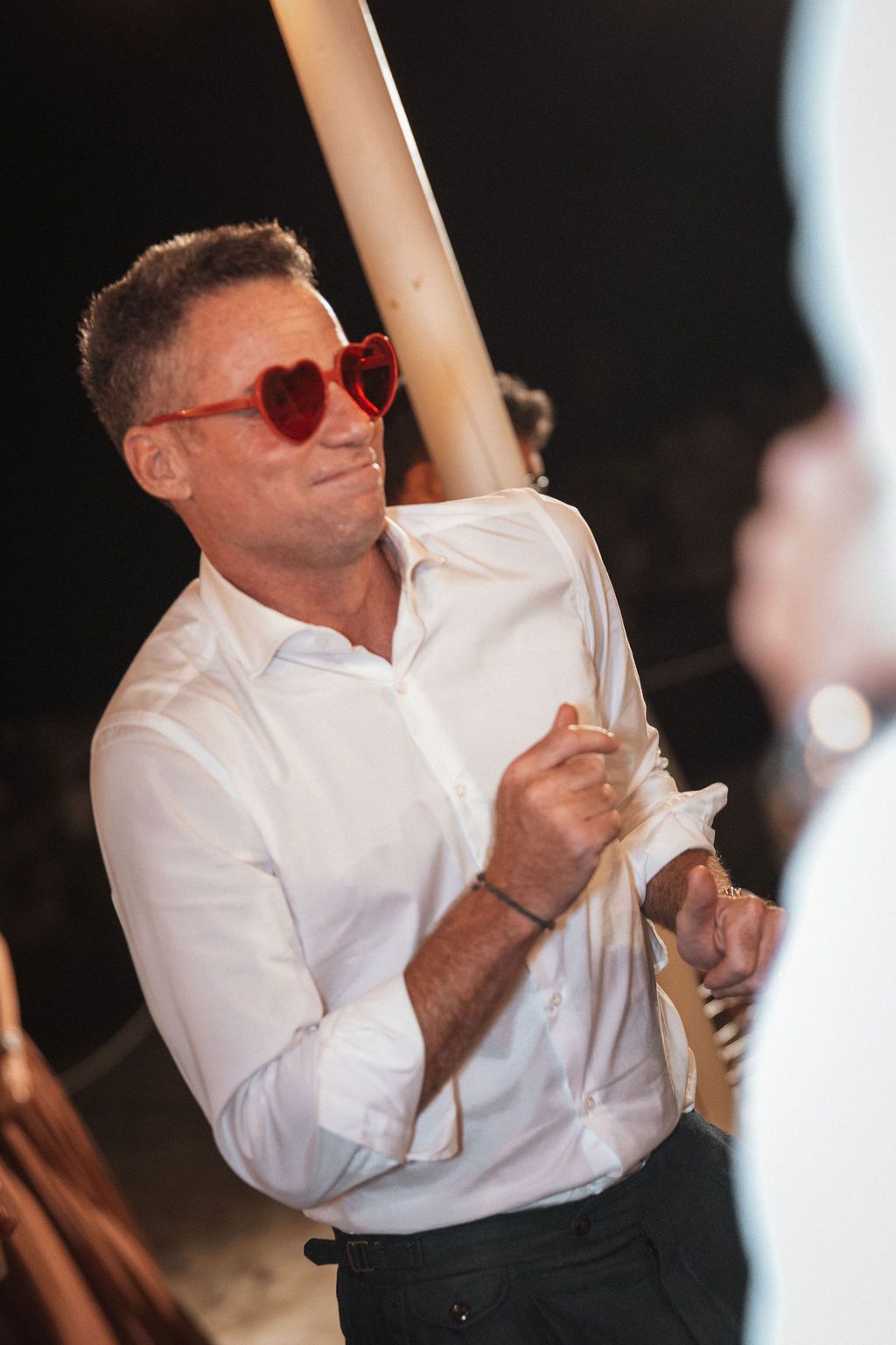 Person in white shirt and heart-shaped sunglasses dancing at celebration.