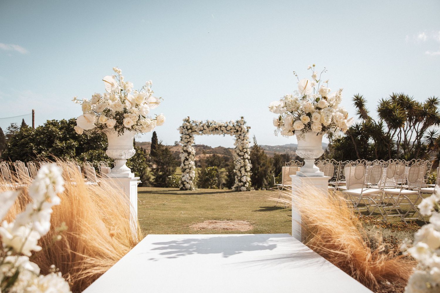 Outdoor wedding ceremony setup with pampas grass and floral arrangements against blue sky.