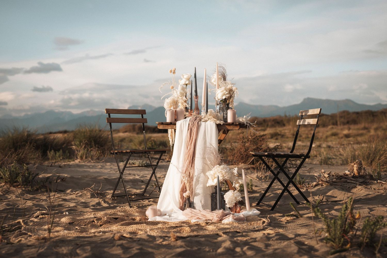 Rustic outdoor wedding setup with folding chairs and draped fabric against mountain landscape.