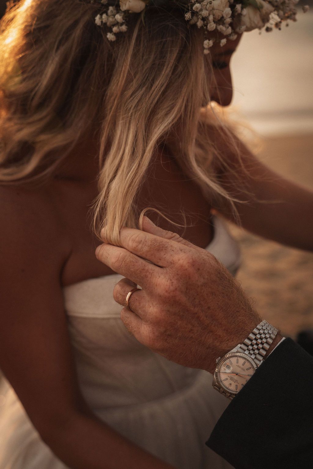 Close-up of hand with watch and ring touching white dress fabric adorned with baby's breath flowers.