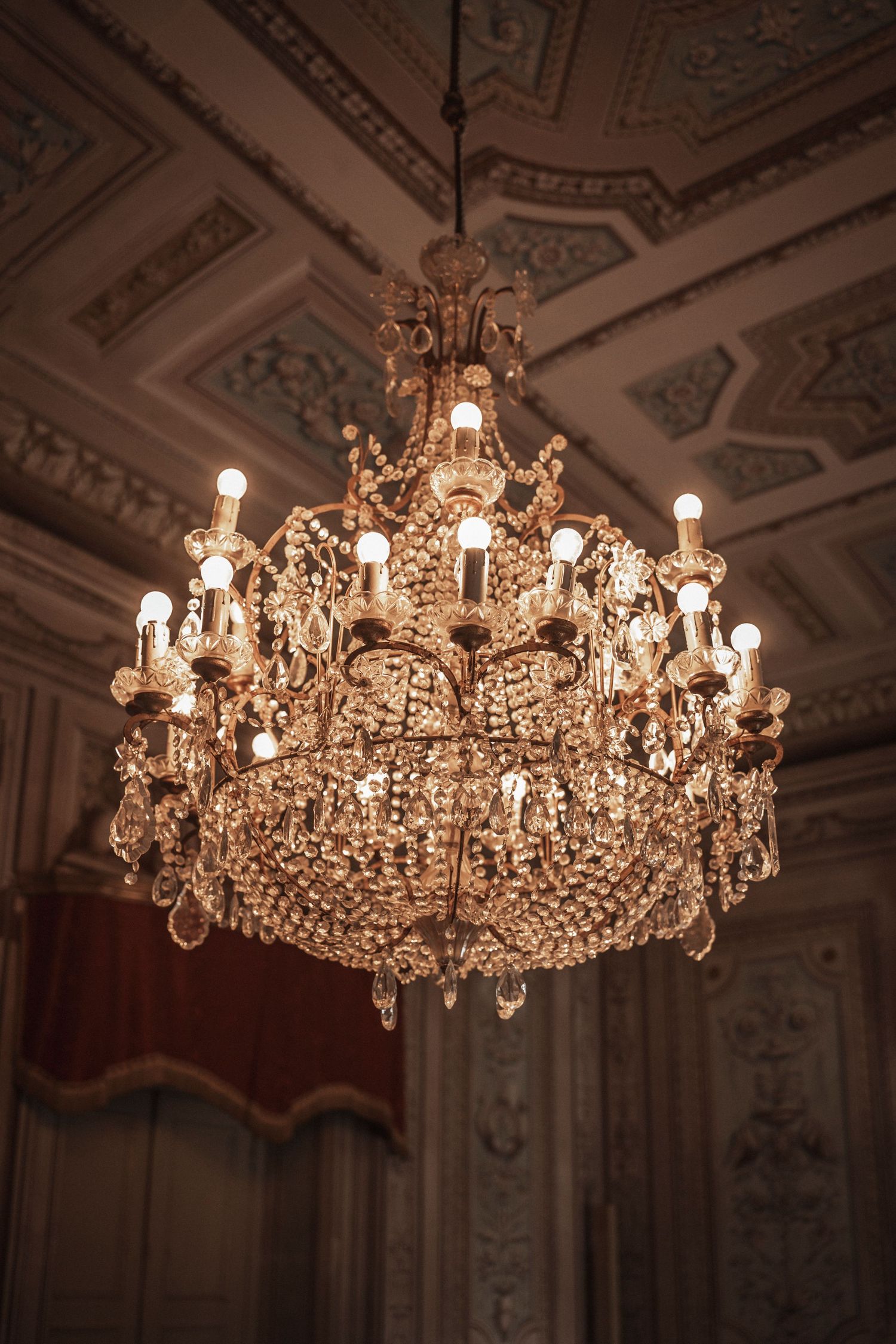 Ornate crystal chandeliers hanging from an elegant decorated ceiling in a ballroom.