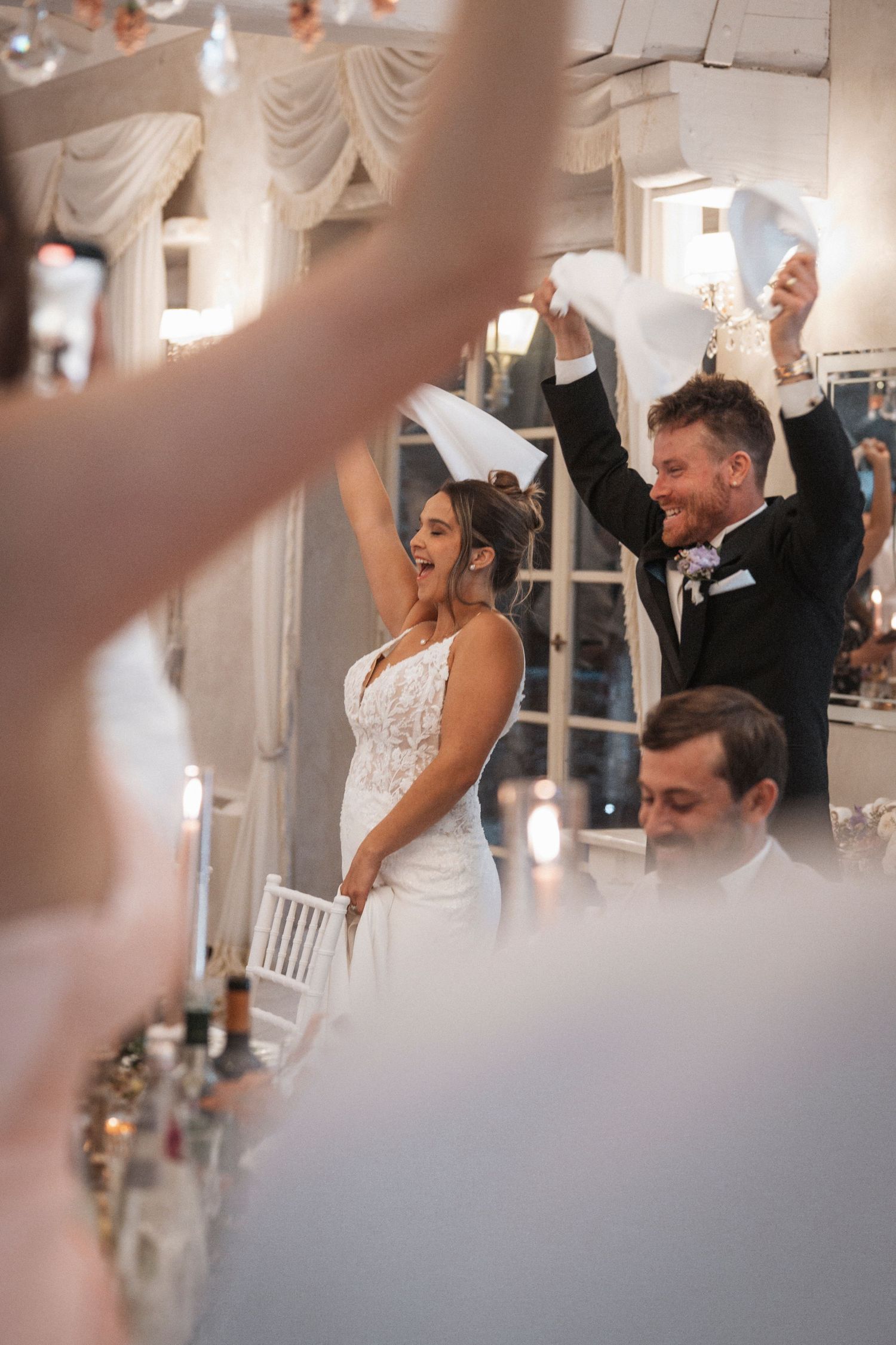 Wedding reception celebration with guests waving napkins in a decorated banquet hall.