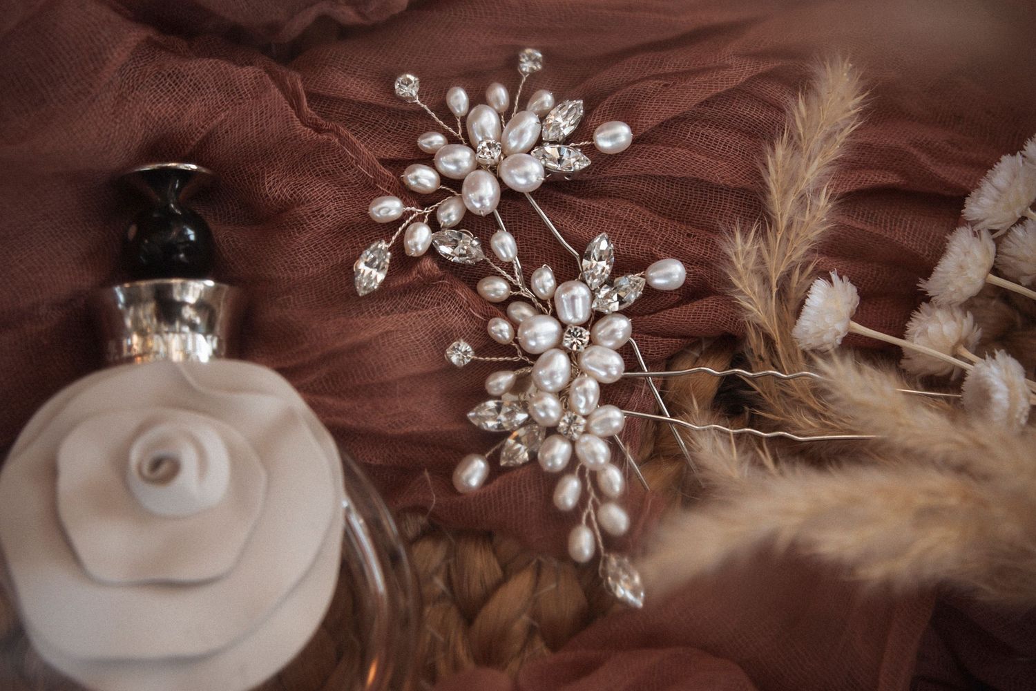 Pearl and crystal bridal hair accessories with dried pampas grass against brown fabric background.