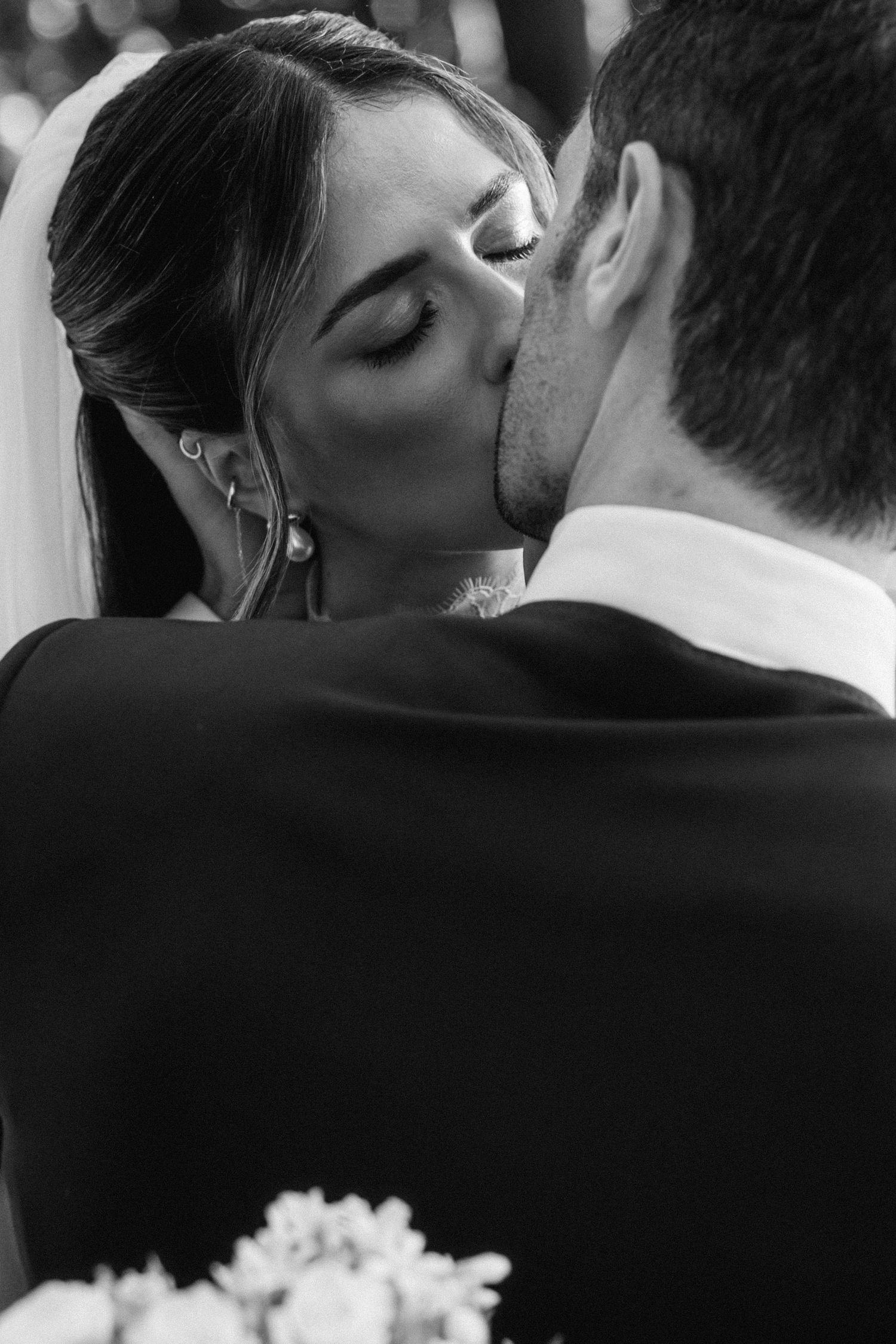 Black and white photo of a bride and groom sharing their first kiss at the wedding ceremony.